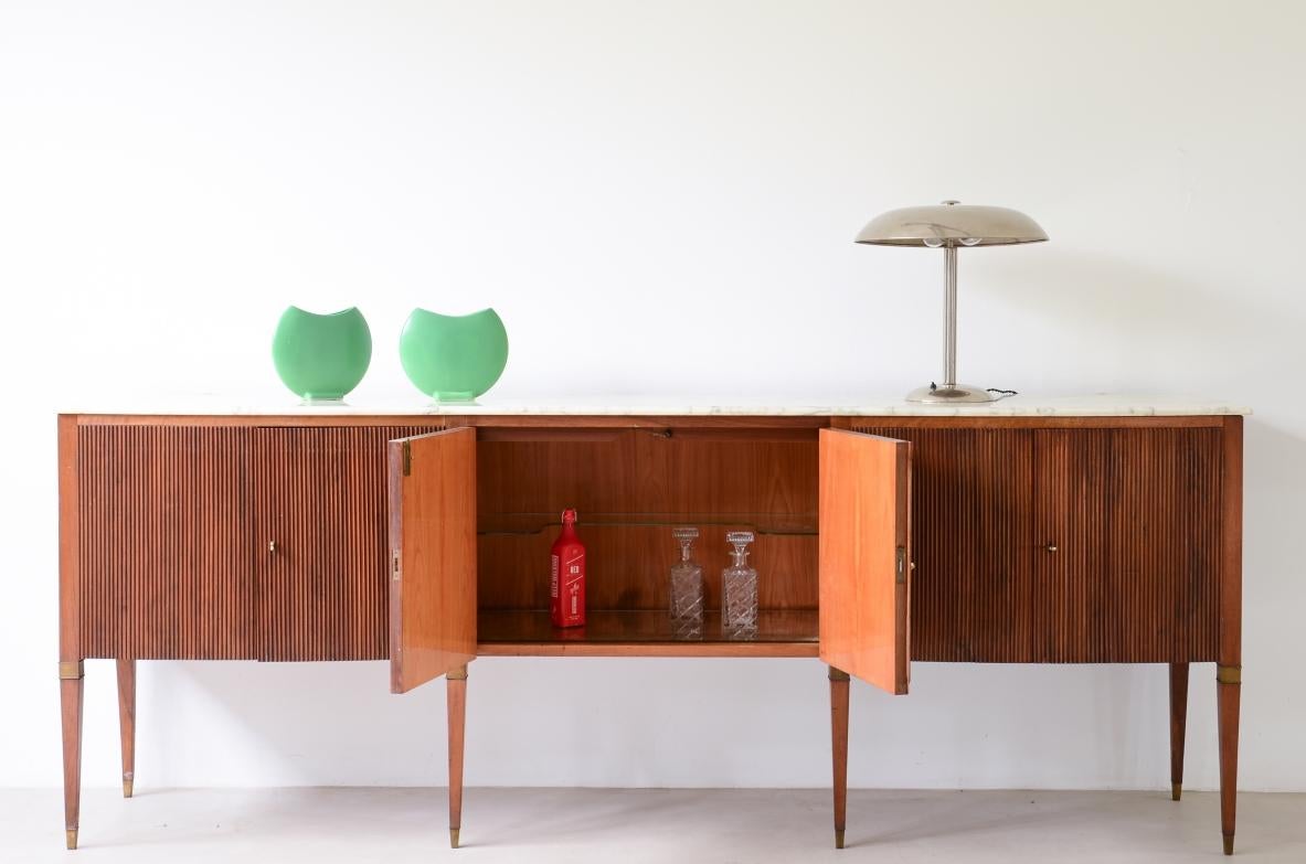 Attributed to Paolo Buffa (1903-1970)

Splendid sideboard with a wavy front, six doors in reeded walnut and six legs with brass capitals and tips, a Bardiglio marble top and a bar with a mirror and a shaped shelf in ground glass.

Manufactured by