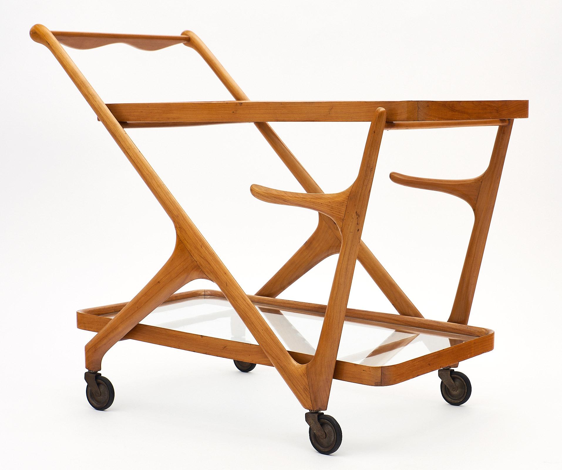Italian bar cart in the manner of Paolo Buffa. This piece is made of solid, high-quality birch wood with a dynamic modernist structure. There are two glass shelves, and the cart rolls on original working casters. We love the small tray and