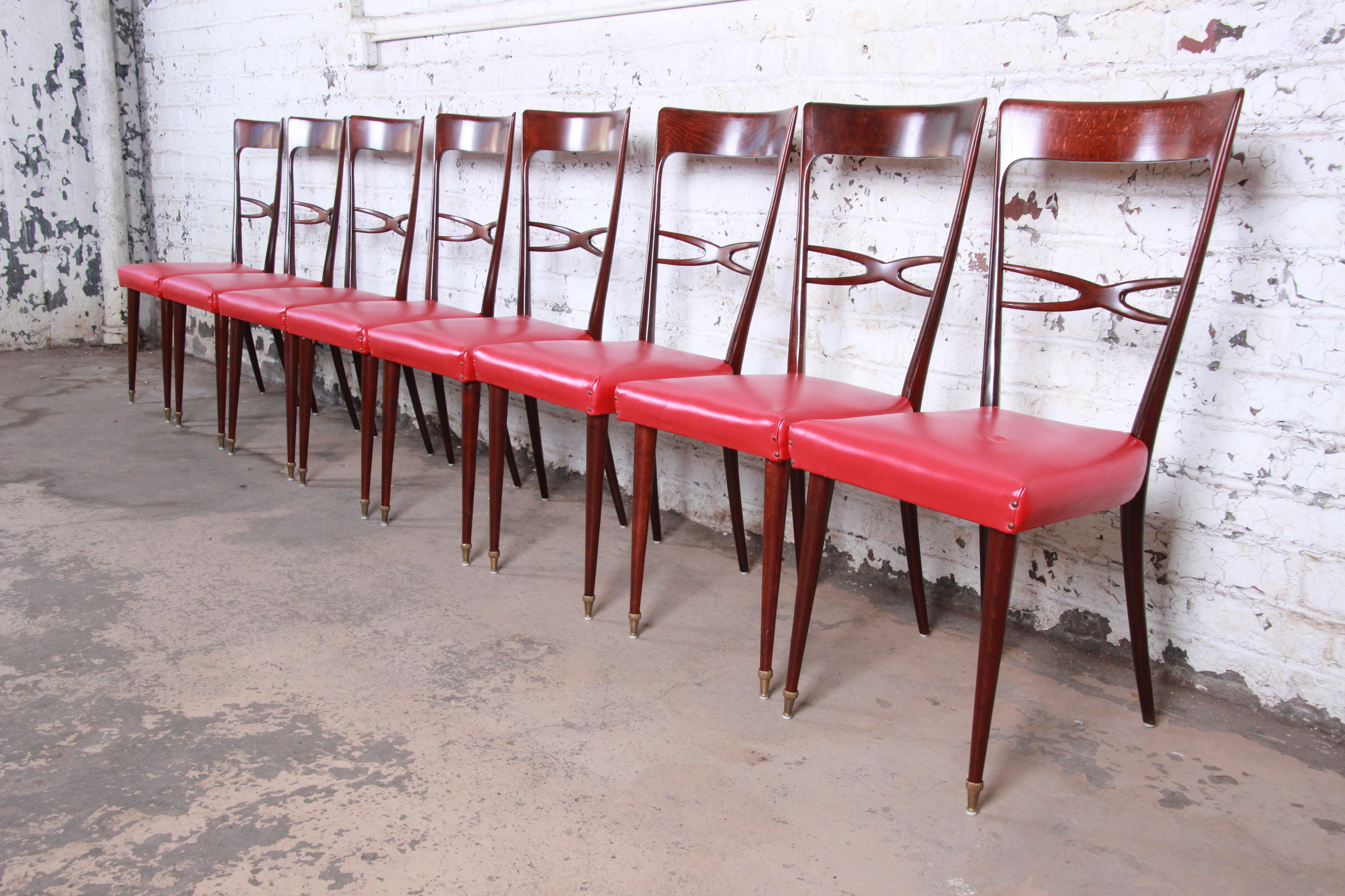 A gorgeous set of eight midcentury Italian Modern dining chairs in the style of Paolo Buffa. The chairs feature petite sculpted dark maple frames with tall tapered legs and brass-capped feet. The studded red vinyl upholstery could be used as is or