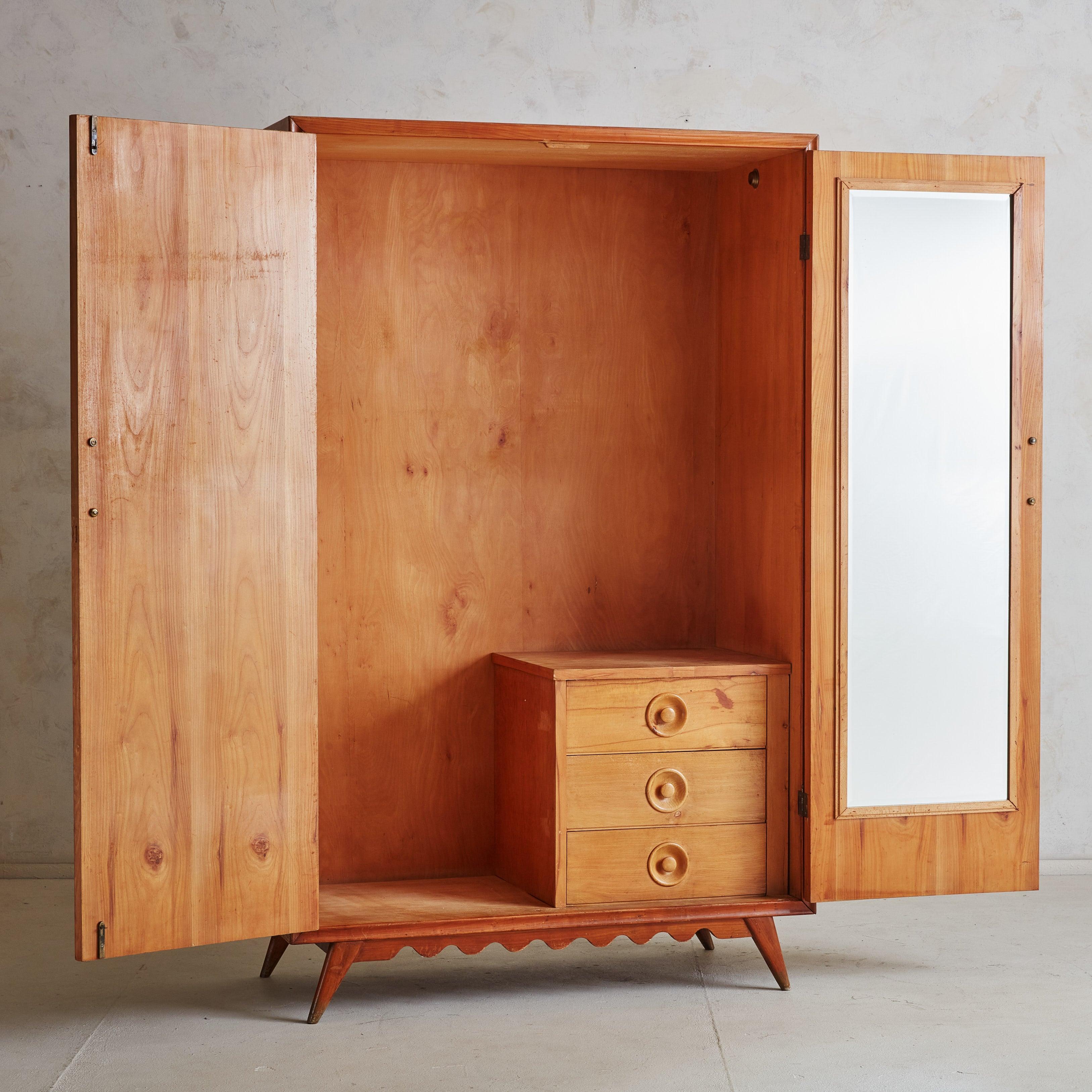 A gorgeous 1940s armoire cabinet reminiscent of designs by Italian architect and furniture designer Paolo Buffa. The monumental silhouette is composed of waxed wood in a rich cherry hue and features sculptural glass handles secured with brass