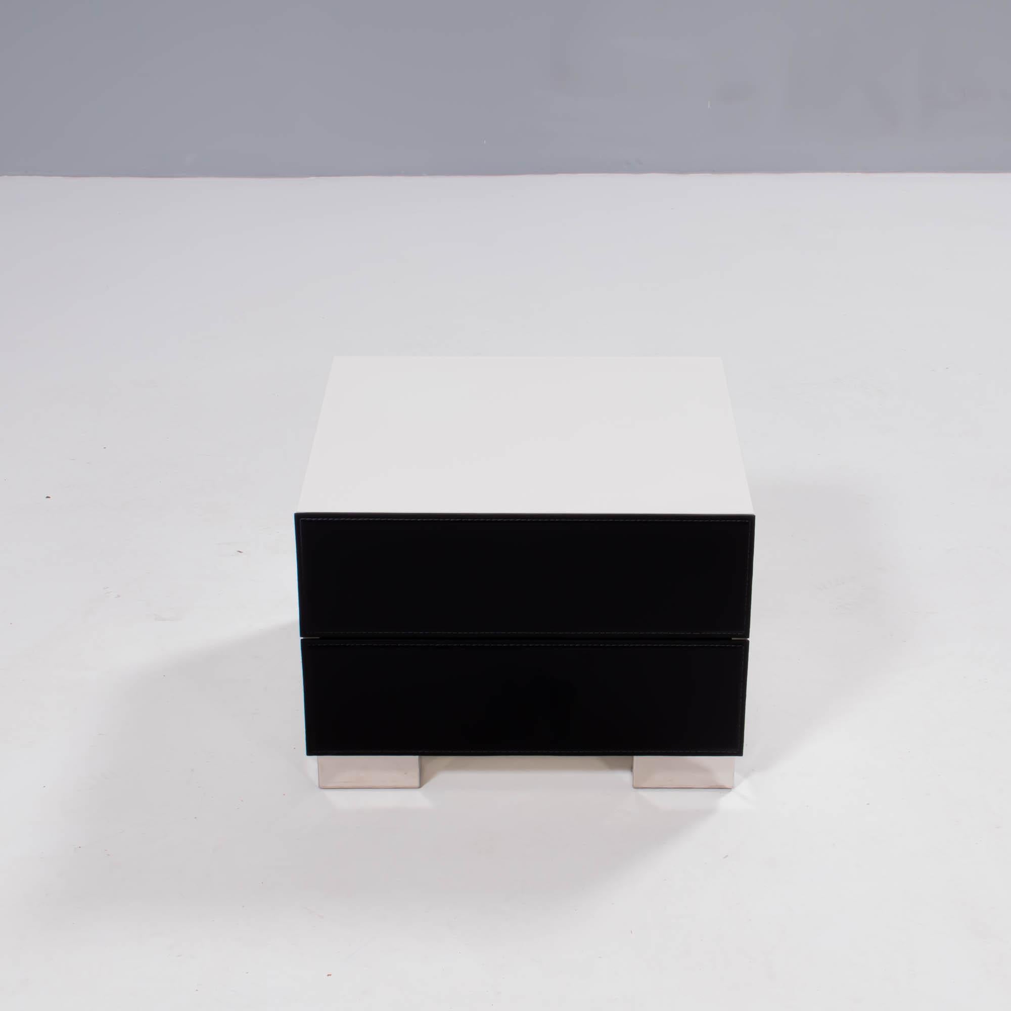 Designed by Paolo Cattelan in 2004, the Dandy bedside table is a sleek contemporary design.

Constructed from white lacquered wood, the bedside table features two drawers with black leather fronts, finished with seam detailing.

The stainless