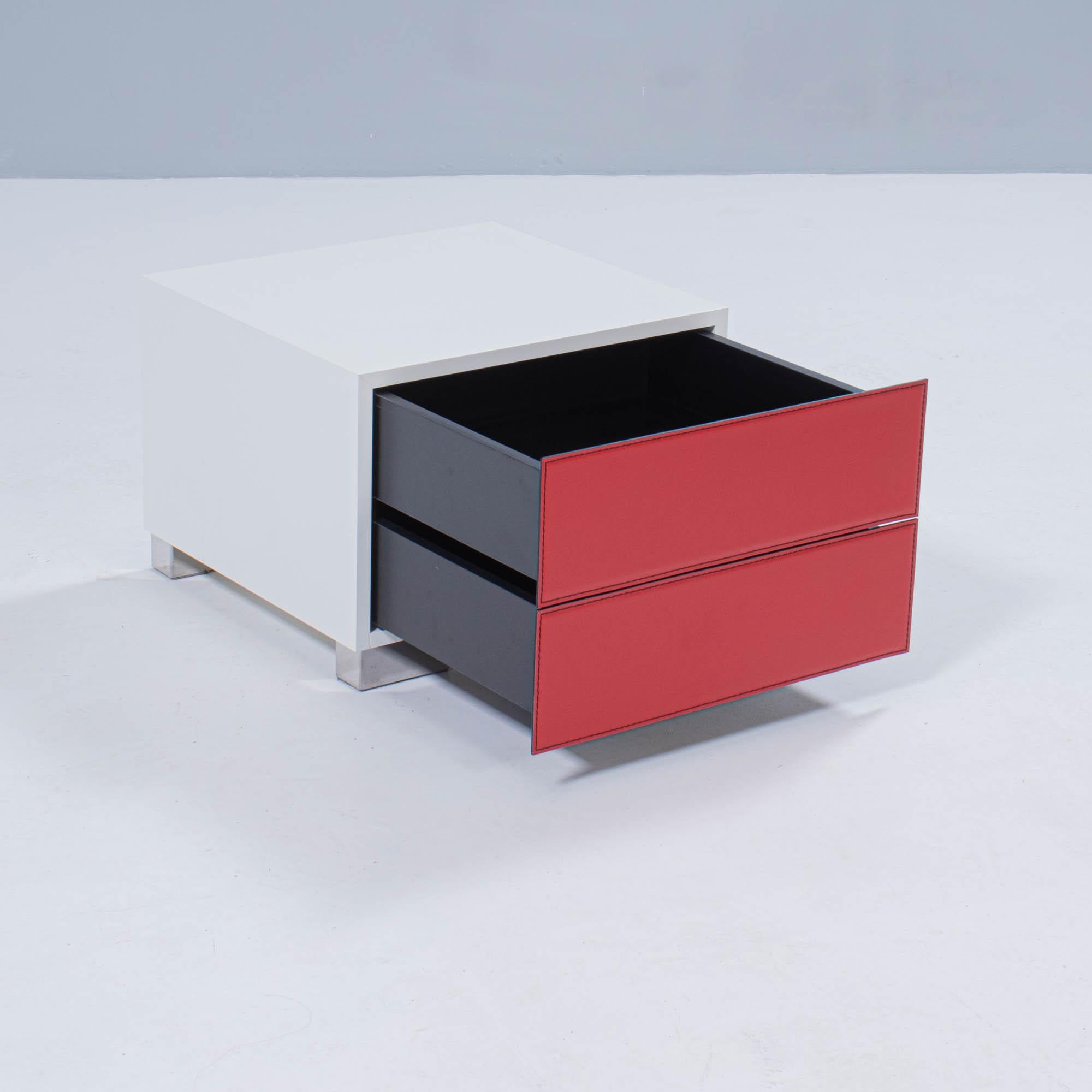 Designed by Paolo Cattelan in 2004, the Dandy bedside table is a sleek contemporary design.

Constructed from white lacquered wood, the bedside table features two drawers with red leather fronts finished with seam detailing.

The stainless steel