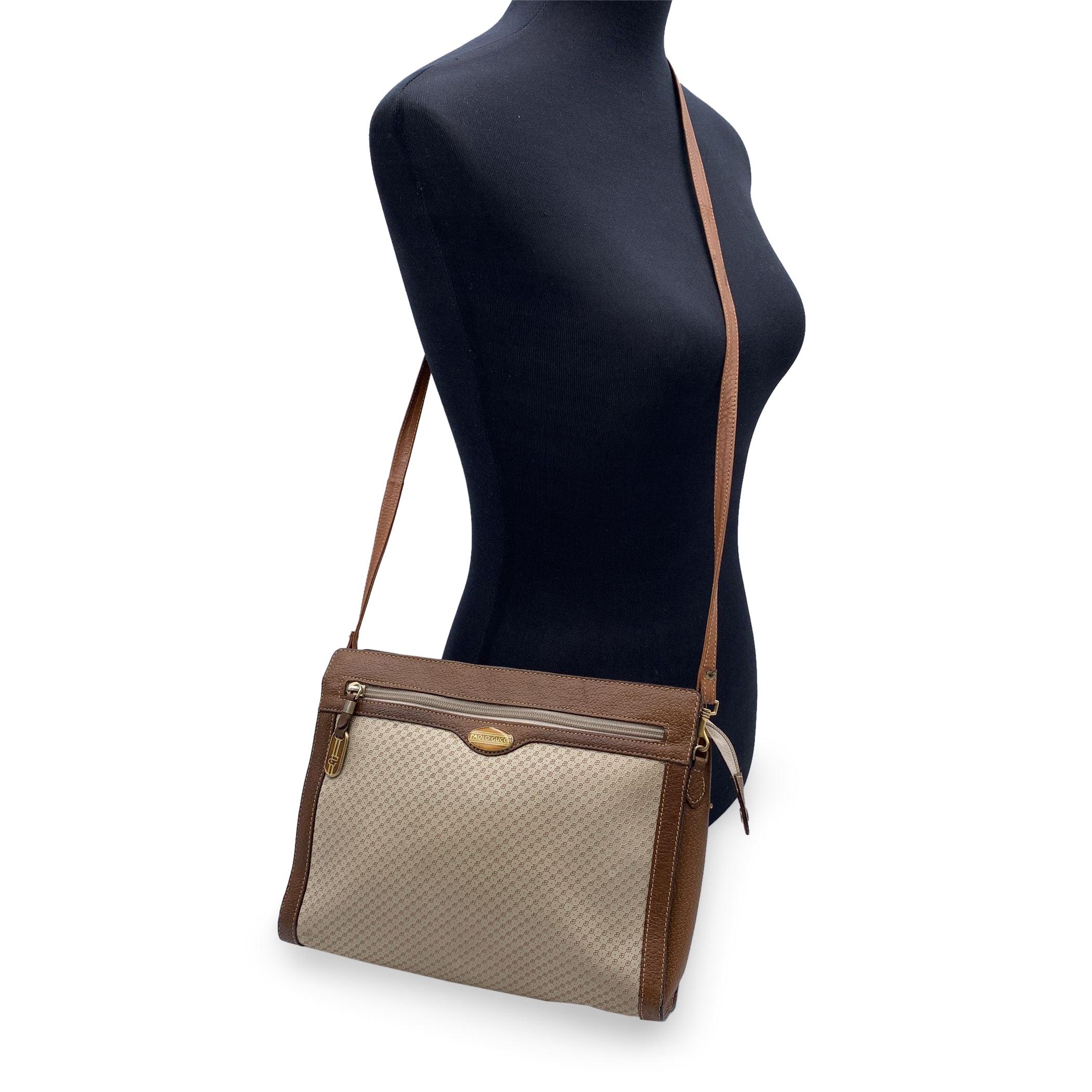 Borsa a tracolla vintage Paolo Gucci in tela vinilica beige chiaro con finiture in vera pelle marrone e tracolla. Logo PG in rilievo su tela vinilica. 1 tasca frontale con zip. Linguetta con logo smaltato Paolo Gucci sul davanti. Chiusura superiore