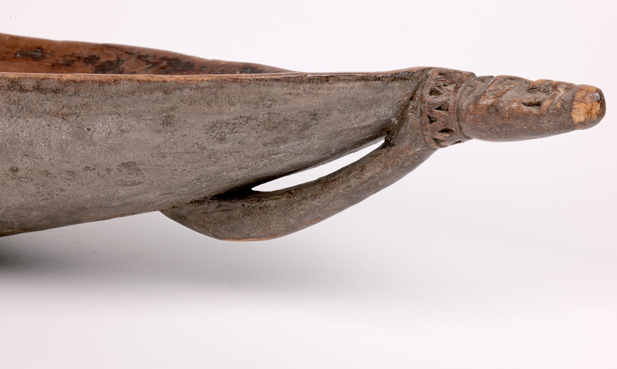 A stunning and large antique tribal carved wooden feast bowl originating from Papau New Guinea and dating from the early 20th century. The bowl is hand chip carved in a light wood and is of long elliptical form resting on a small flat round foot and