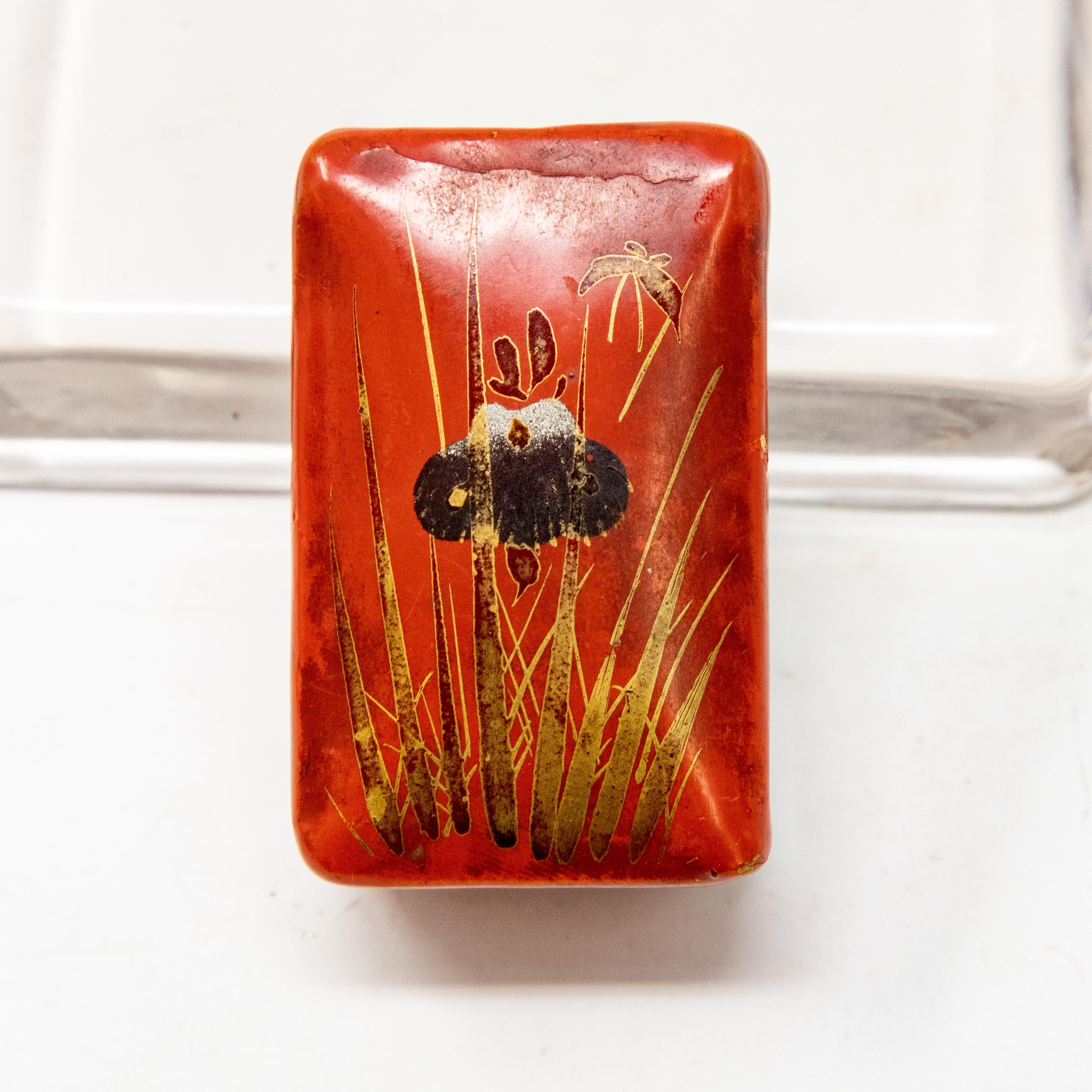 Offering this stunning red lacquered papier mâché pillbox. The bottom and inside of the box are black lacquer. The front is hand painted and has an orchid with other foliate designs.