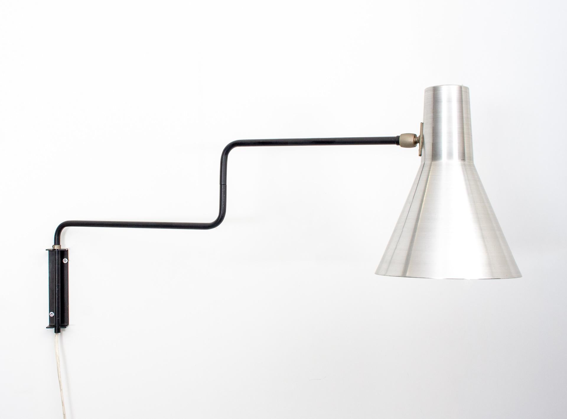 Very nice wall lamp, model 71-01 named Elbow or Paperclip, designed by J.J.M. Hoogervorst in 1958 for Anvia.
The lamp is fully adjustable by the arms as well as the shade. It has Black arms and a Polished Aluminum shade. The lamp is in very good