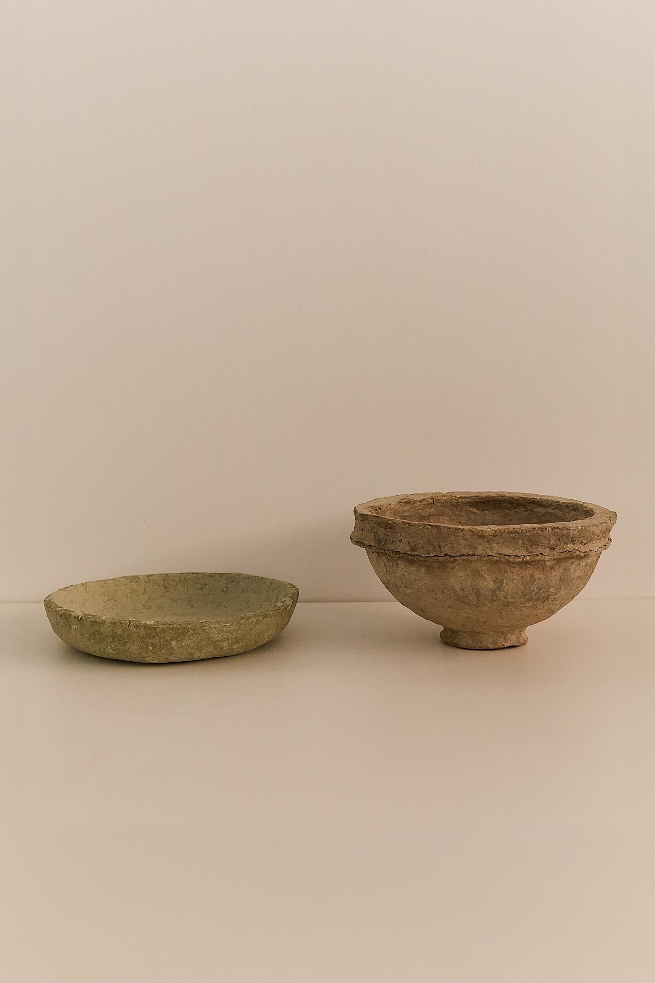 A unique pair of hand-formed bowls crafted from papier-mâché, each with a richly textured surface and sculptural form. One features a shallow, open shape, while the other is footed with a stepped profile; together evoking a raw, primitive elegance.