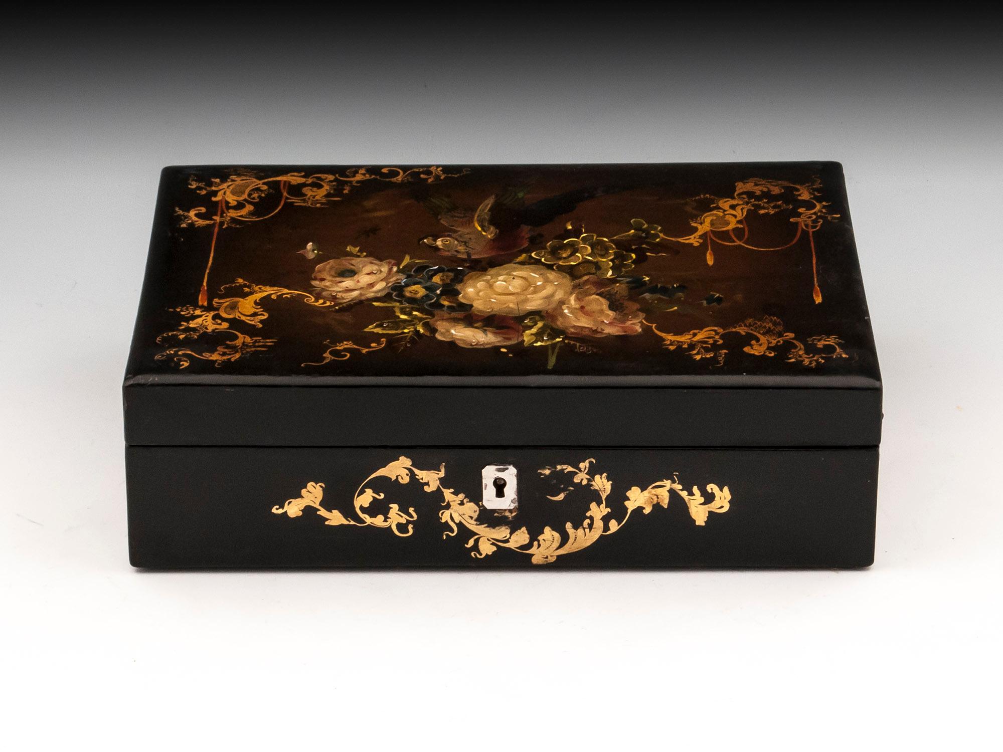 Papier mâché sewing box beautifully adorned with flowers and an exotic bird, framed by gold floral sprays which continue around the lock escutcheon. 

The interior of this papier mâché sewing box is lined in green velvet and patterned paper and is