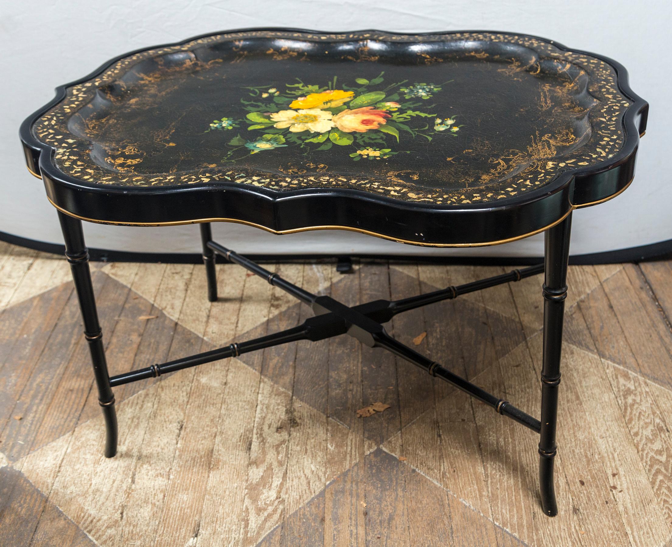 A shaped black papier mâché tray with inlays of mother of pearl around the outer raised edge. Worn gilt decoration within the outer edge of the tray area. The center with hand painted flowers and leaves.
Raised on a custom made 