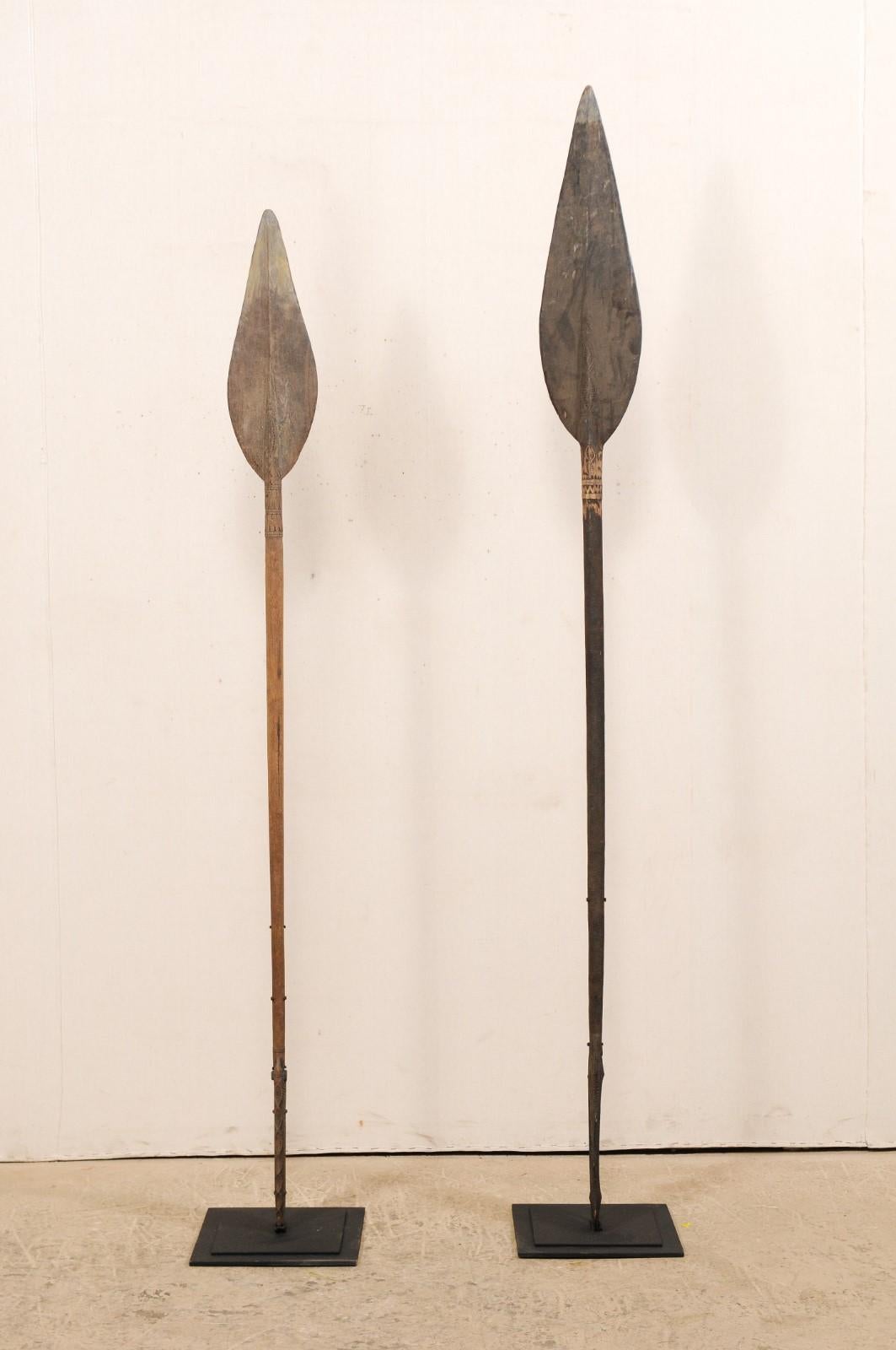 A pair of vintage Papua New Guinea carved wood canoe steering paddles on custom stands. This pair of carved wood paddles originate from along the Sepik river regions of Papua New Guinea. These river and oceanic pieces have spear-like tips at one