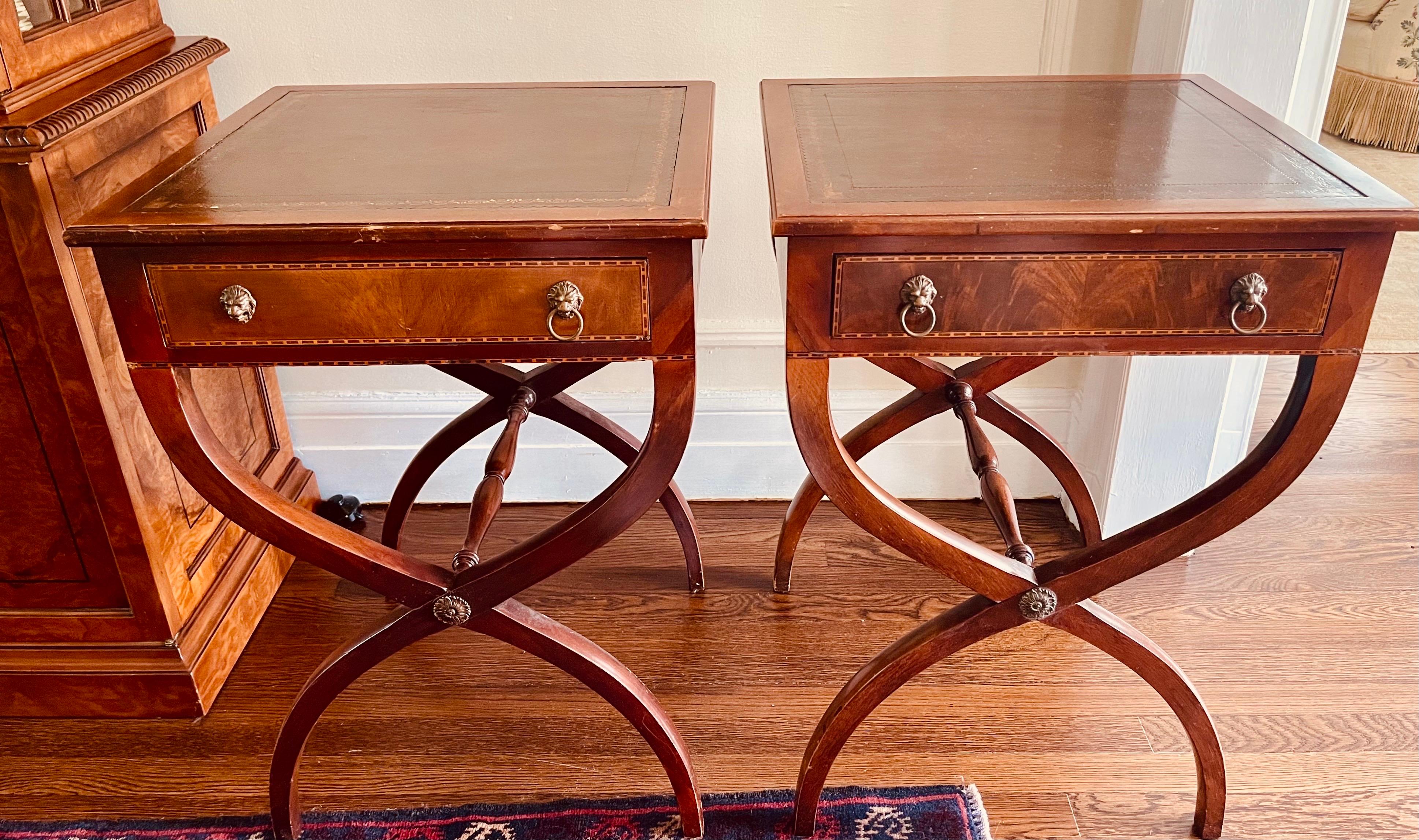 Exquisite pair of regency style rare mahogany one drawer end tables with leather tops supported on x-base crossed saber legs. Features brass lion door pulls. Circa late 19th century.