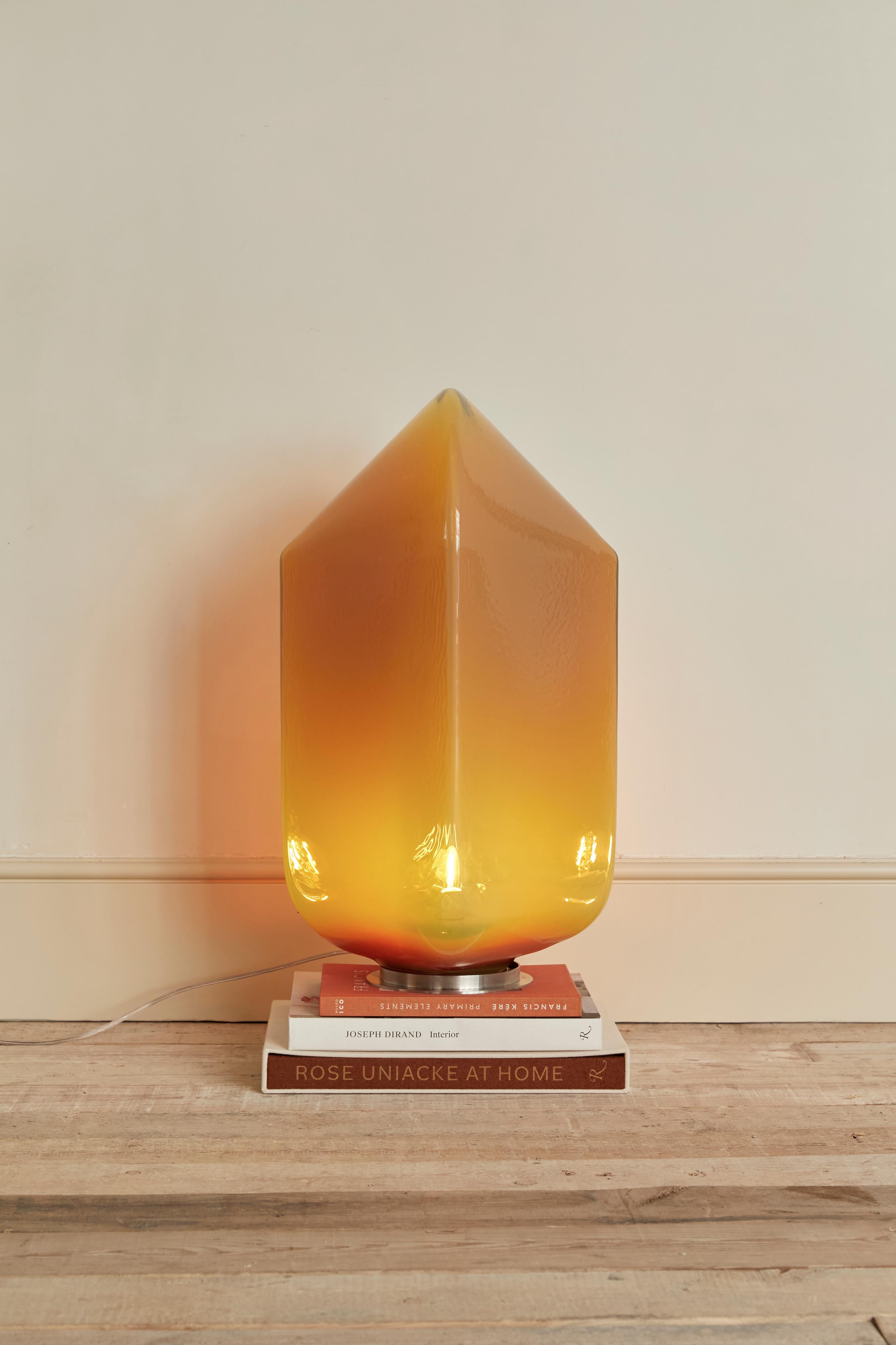 Glastischlampe des Künstlers Jonas Trampedach. Diese große Lampe wird in der dänischen Glashütte Holmegaard mit der Technik des Durchblasens eines Rohres hergestellt. Die Menge der eingeblasenen Luft bestimmt die Größe des Objekts, jedes Stück wiegt