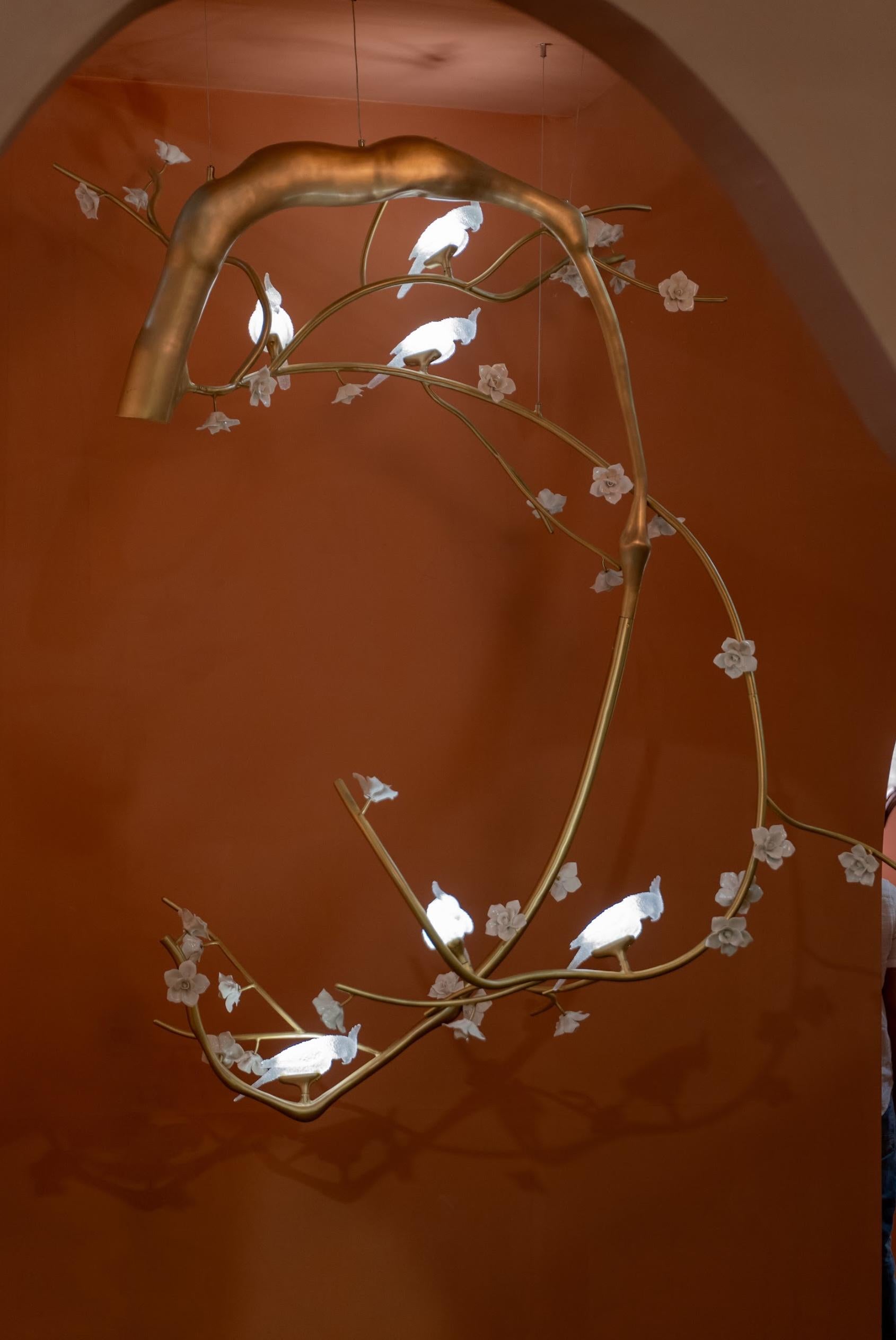 Il lampadario nell'immagine è uno squisito apparecchio di illuminazione ispirato alla natura che fonde splendidamente arte e funzionalità. Il design ricorda un ramo d'albero graziosamente curvo, realizzato con una calda finitura metallica dorata che