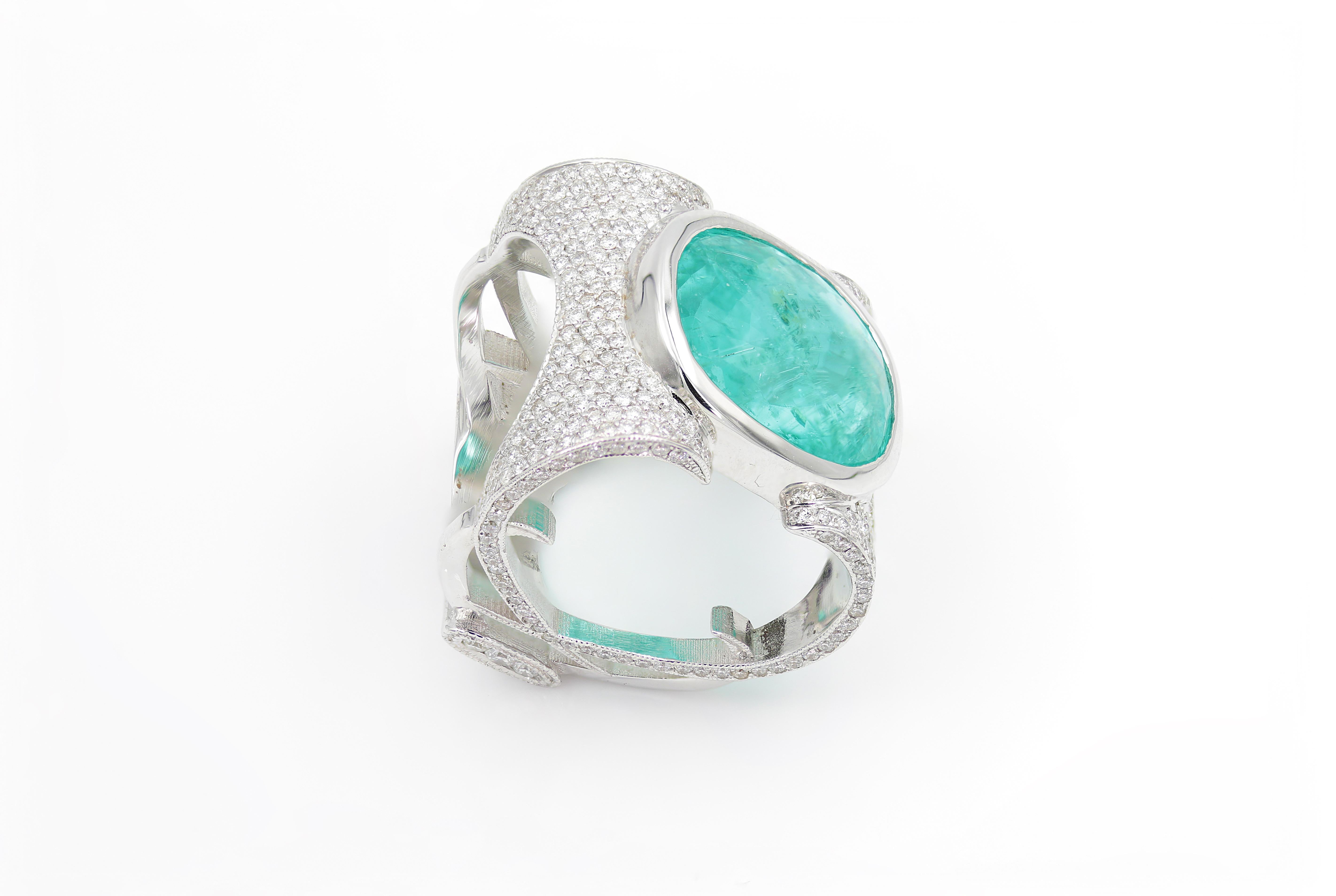 Elevate your evening look with this stunning cocktail ring! Set in a bezel setting with a 14k White Gold band is a rare 18mmx15mm 14.98 carat Paraiba Tourmaline gemstone with an oval cut. The decorative band is encrusted with approximately 400 G