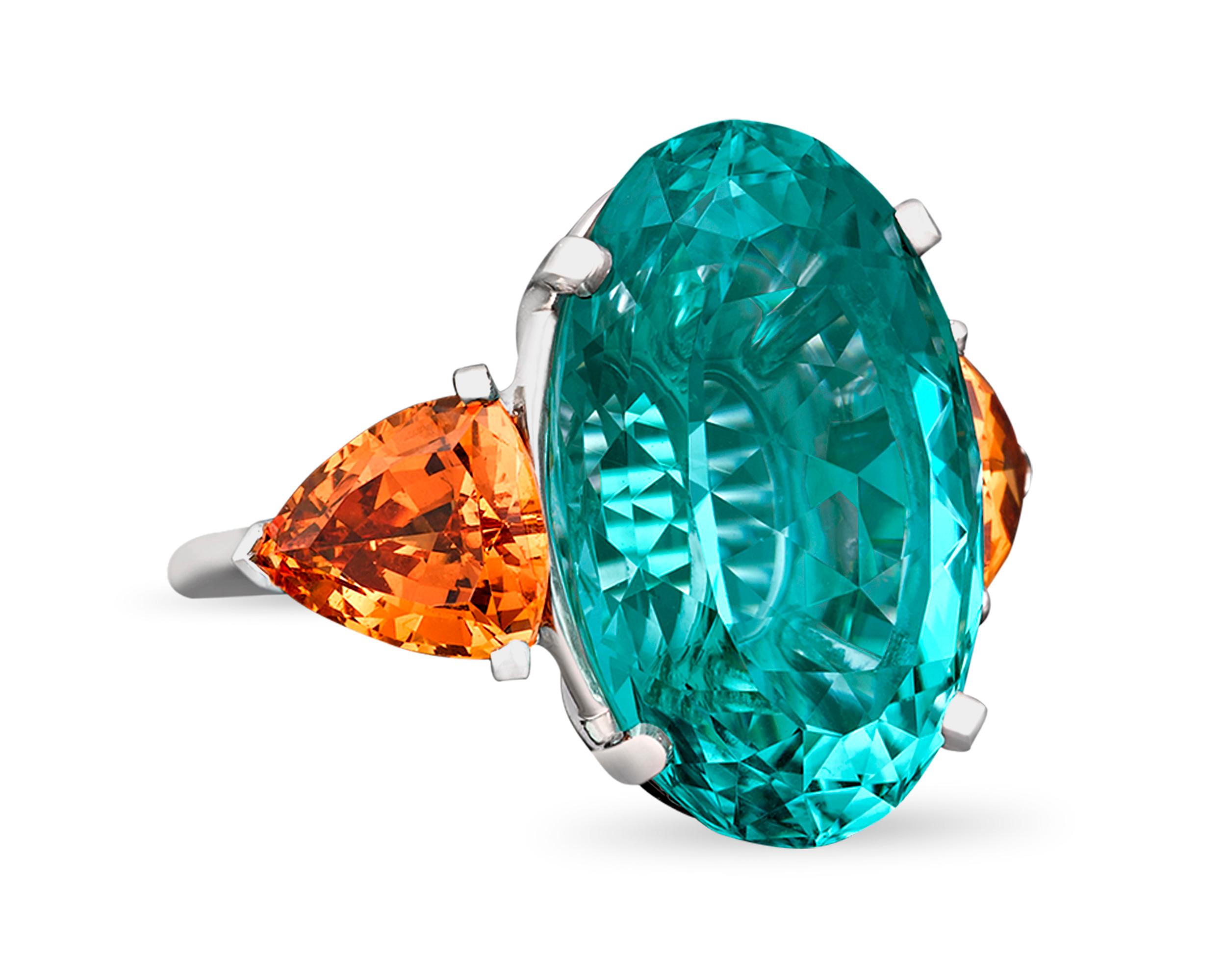 A pair of rare trillion-cut mandarin garnets weighing approximately 5.38 carats and a monumental 22.81-carat oval-cut Paraiba tourmaline make a daring statement in this ring. The fiery orange of the garnet provides an eye-catching contrast to the