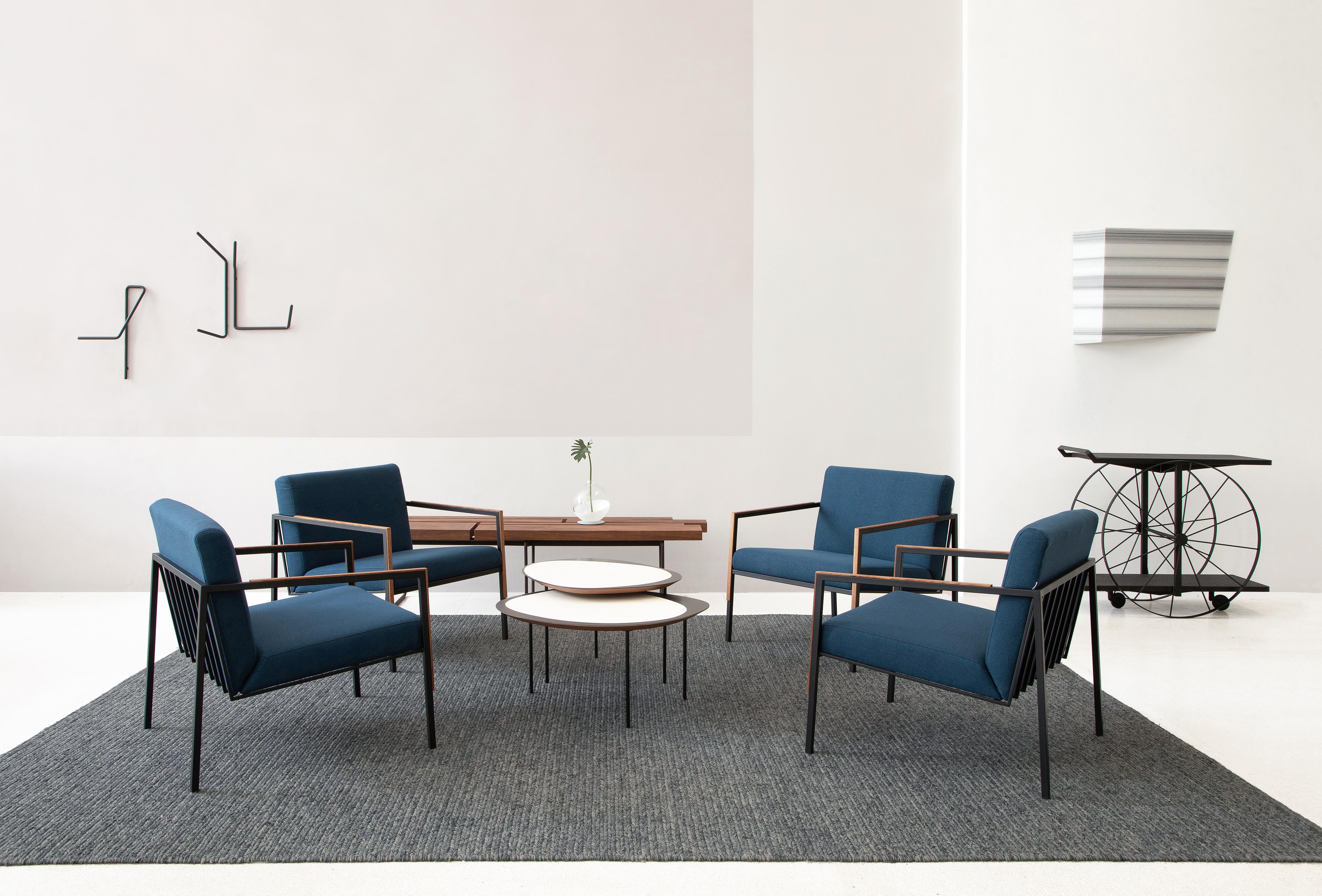 El sillón Paralelas une elementos gráficos y arquitectónicos en su fina estructura metálica con aplicaciones de madera. Tapizados en una combinación de algodón y lino, el asiento y el respaldo contrastan con la ingravidez del metal. Aquí se