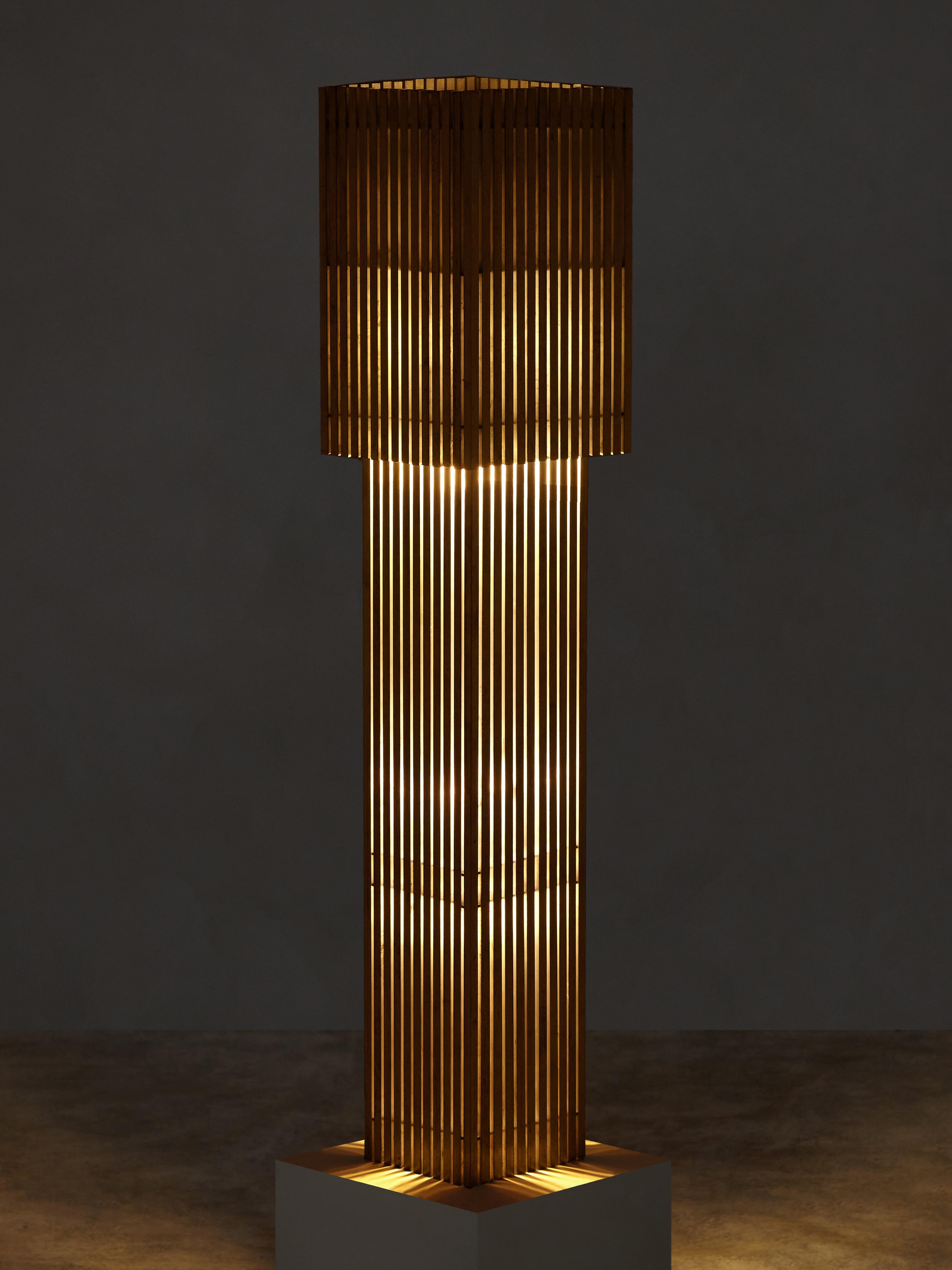 Hand-brushed metal dowels both block and direct the lamp’s concealed LED bulb, casting an uneven glow through the vertical strips of the lamp’s body. The removable top-shade functions as a manual dimmer, allowing the lamp to transform in shape and