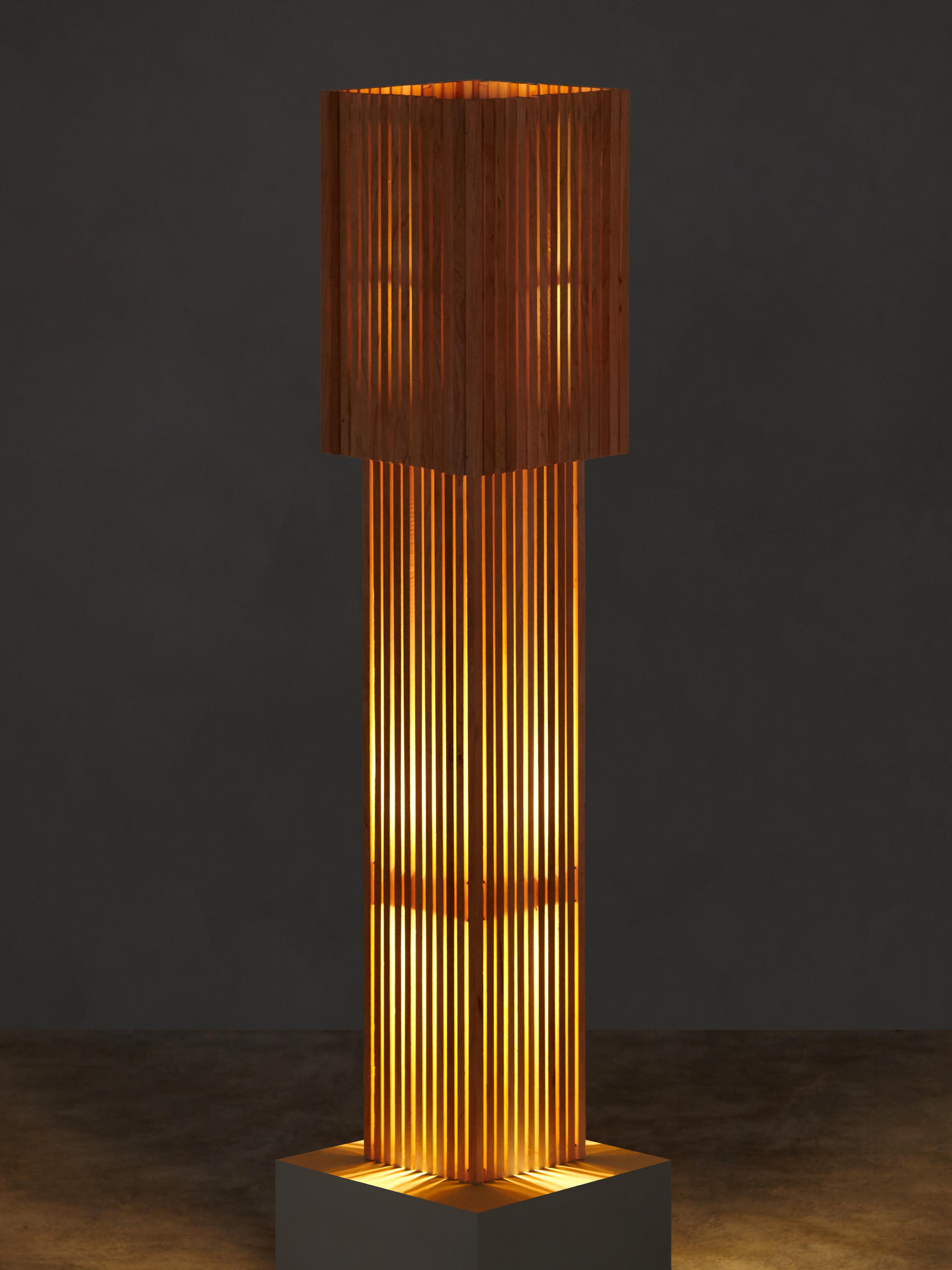 Hand-brushed wooden dowels both block and direct the lamp’s concealed LED bulb, casting an uneven glow through the vertical strips of the lamp’s body. The removable top-shade functions as a manual dimmer, allowing the lamp to transform in shape and