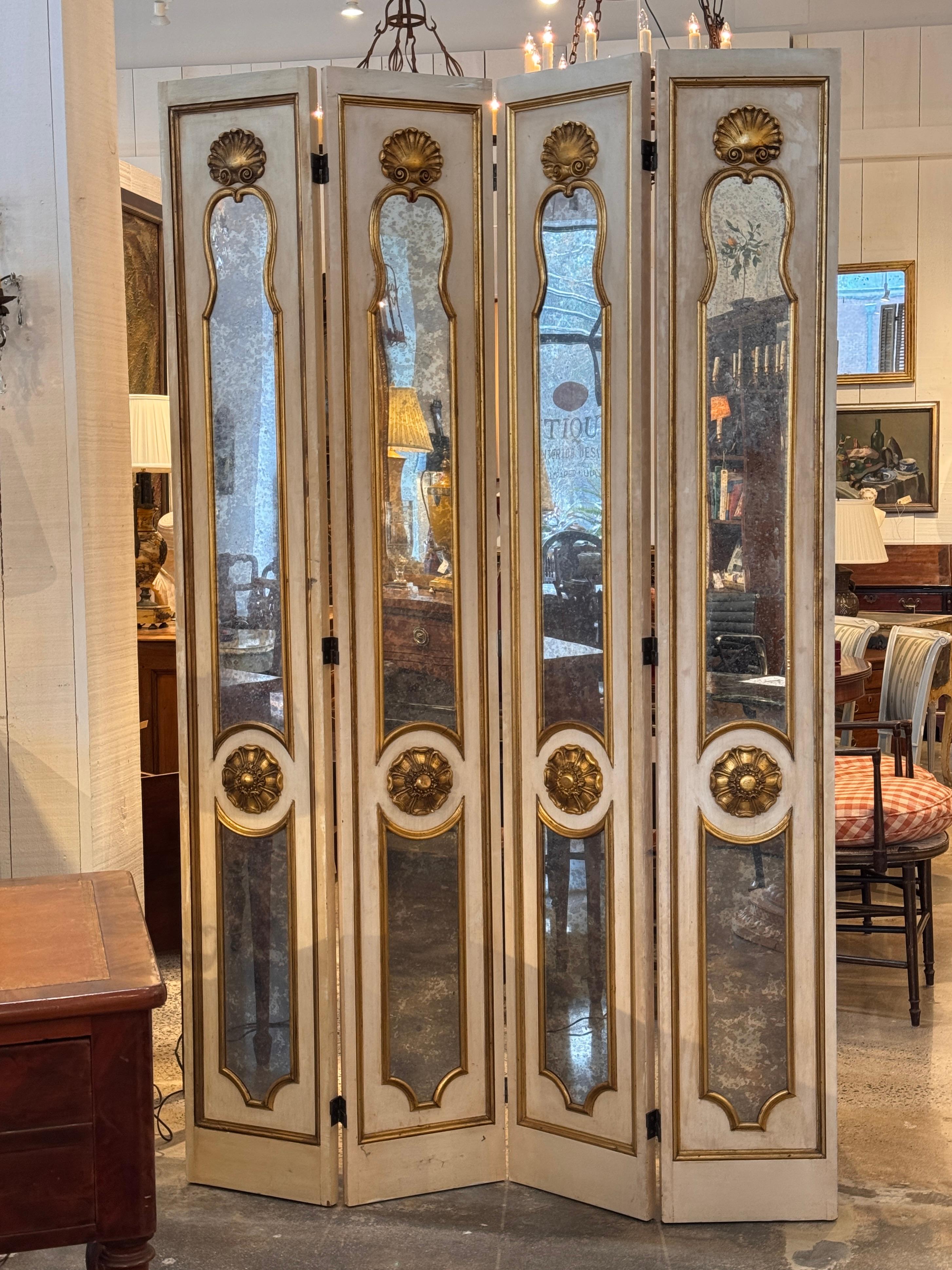 Four-panel screen with parcel-gilt and painted frames surrounding mirrored inserts. Each panel features a shaped gilt border and carved gilt shell and floral medallions, with the mirror plates showing visible aging in the close-up image. Hinges