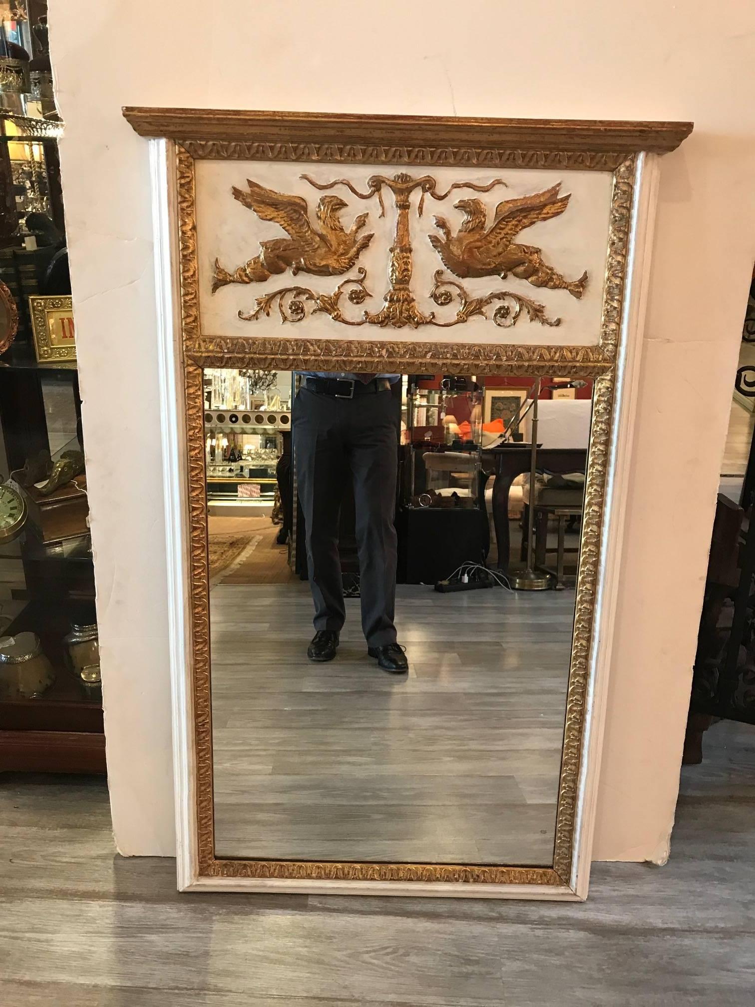 A light cream and giltwood Italian made mirror by Labarge. The upper portion with facing gilt griffins on a cream white background above a mirror with gilt border, marked Made in Italy with an early Labarge label.