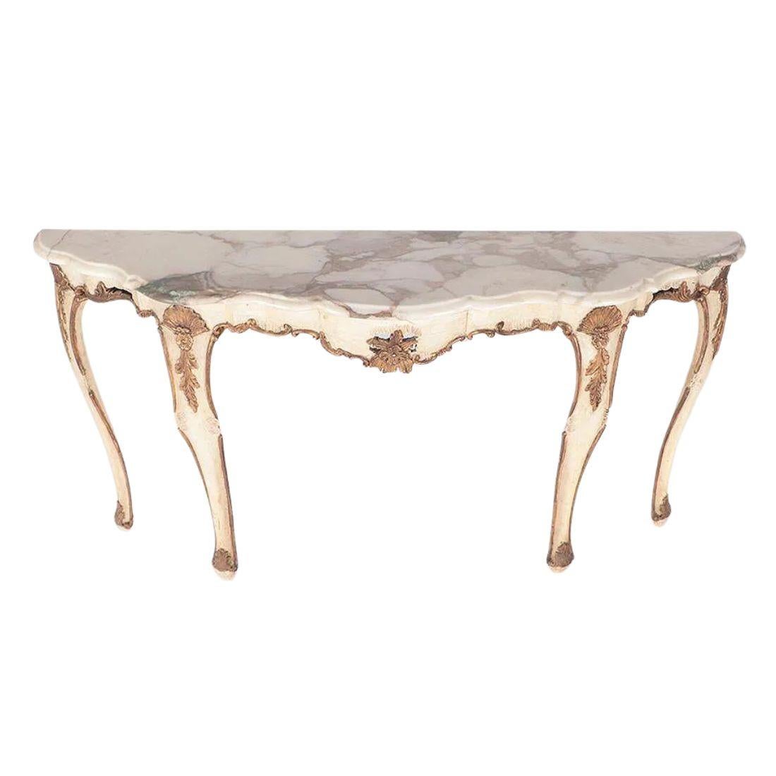 Console en demi-lune à plateau de marbre peint et doré, de style Regency, datant des années 1950. De couleur crème, elle présente de gracieux pieds cabriole, un tablier de forme délicate, des détails de volutes et de coquillages dorés et une base en
