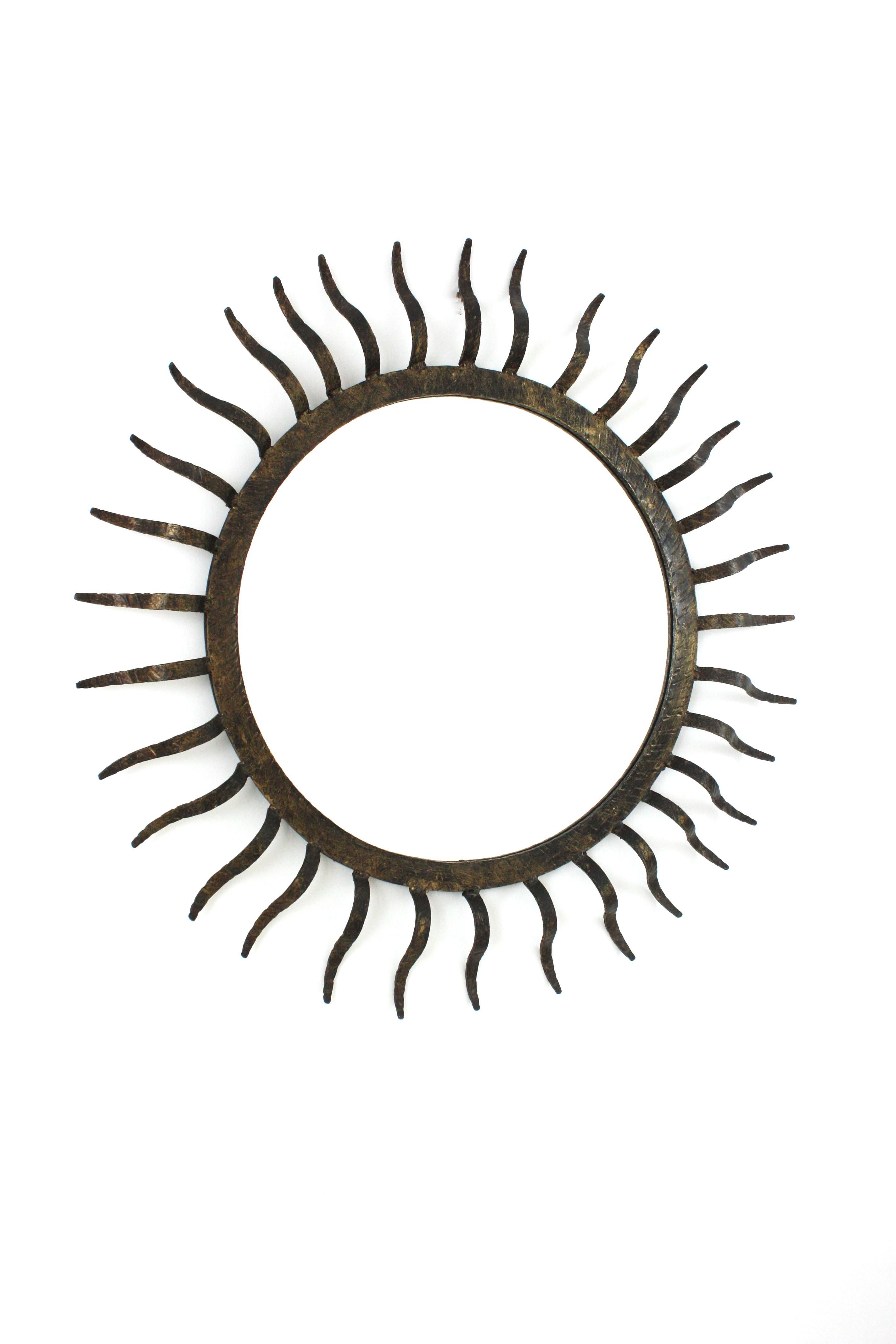 Sunburst mirror in the manner of Gilbert Poillerat, Parcel-Gilt Wrought Iron, France 1940s.
This sunburst wall mirror has an eye-catching sunburst design with iron rays surrounding a central glass. Entirely made by hand in wrought iron. 
The frame