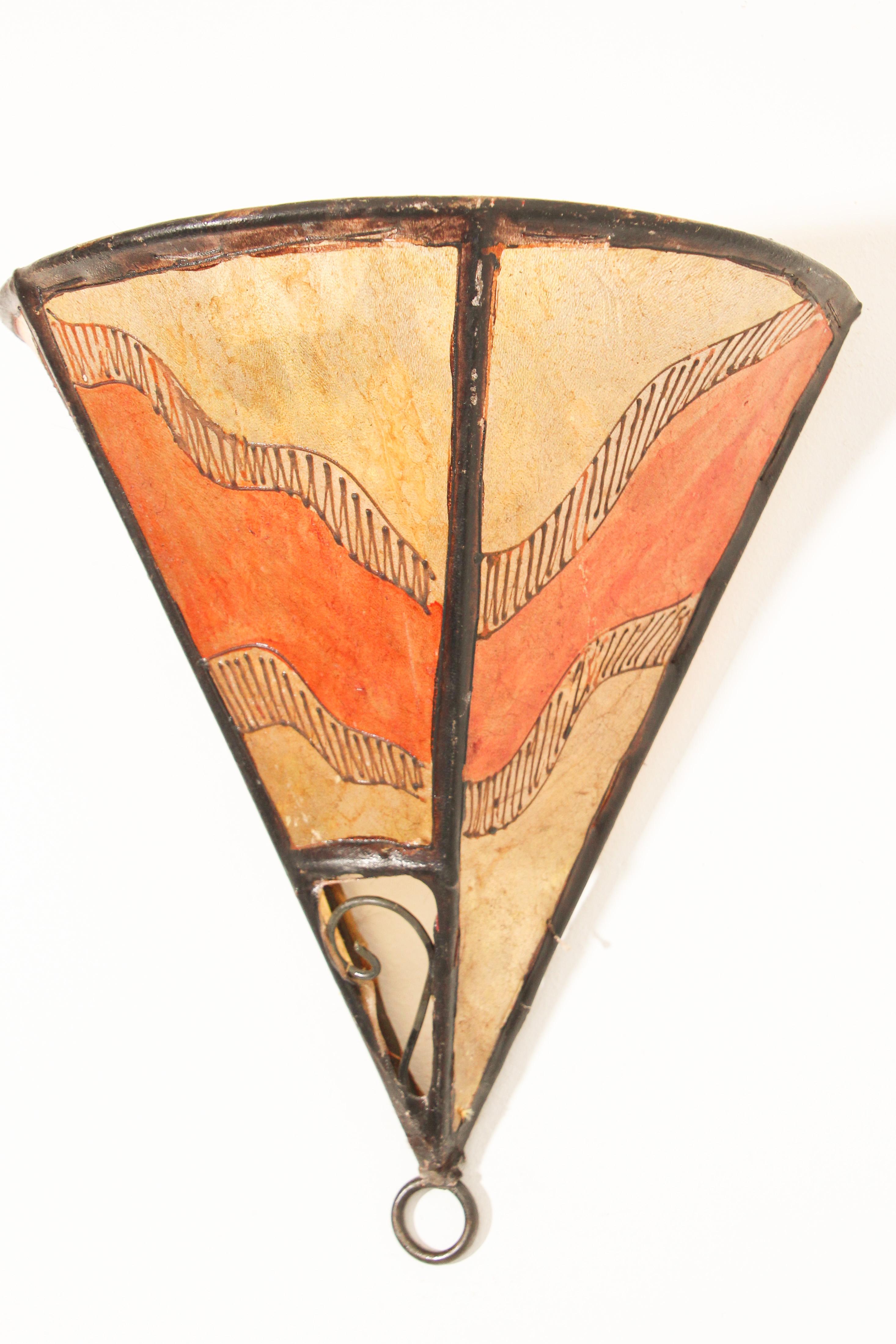 African tribal art parchment wall shade sconce featuring a large triangle hide form stitched on iron and hand painted surface.
These Moroccan art pieces could be used as wall lamp shade.
Iron frame covered with hide parchment which has been hand