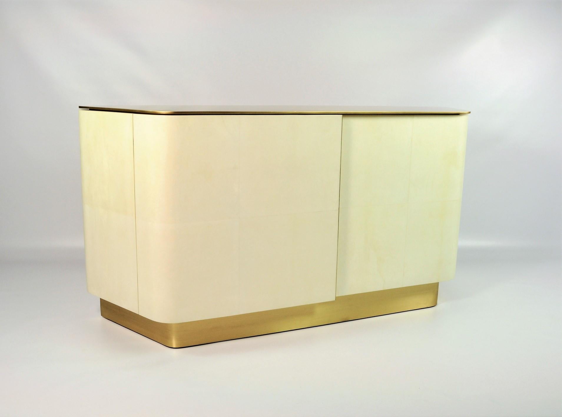 Questo moderno buffet VELA è realizzato in pergamena (pelle di capra).
Ha 2 ante, la parte superiore e la base sono in ottone spazzolato.
Questo pezzo ha un design molto sensuale e moderno.
La pergamena è sbiancata e ha una finitura satinata e