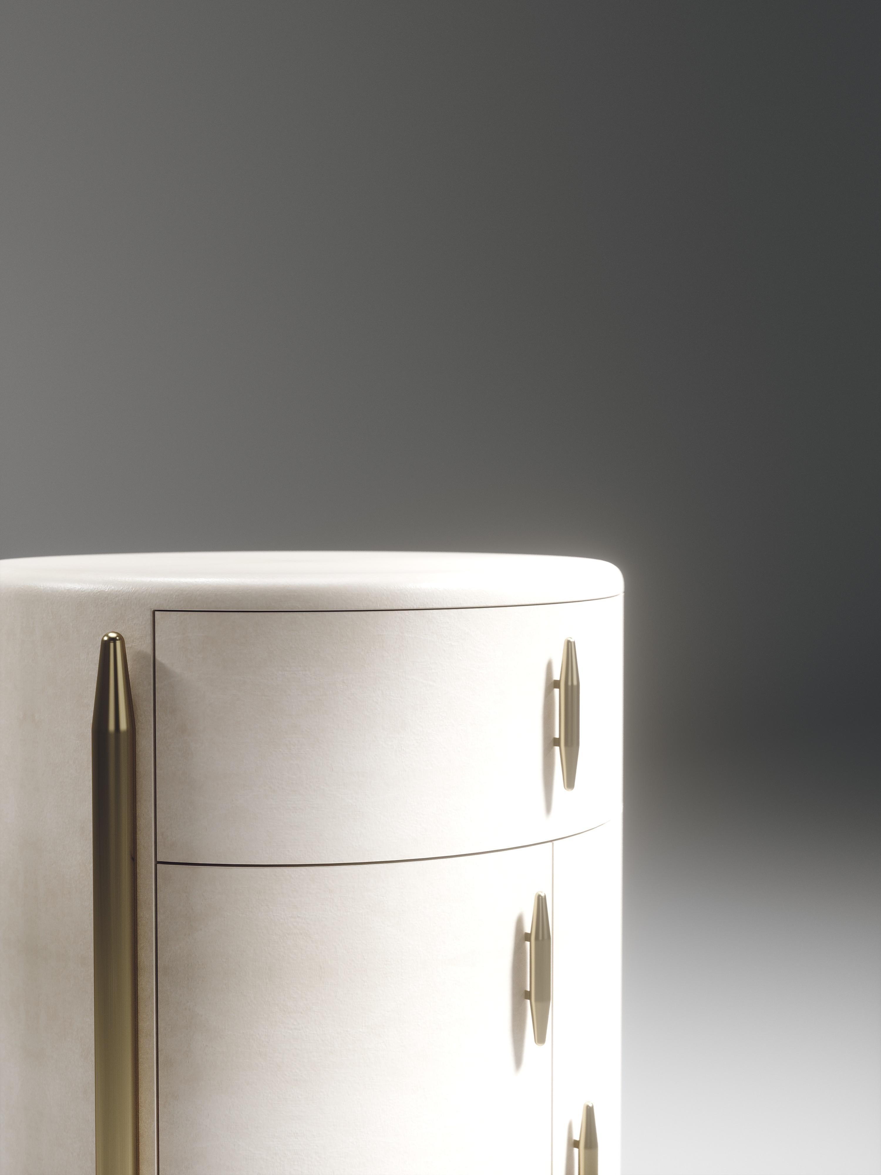 The Dandy round bedside table by Kifu Paris is an elegant and a luxurious home accent, inlaid in cream parchment with bronze-patina brass details. This piece includes 1 drawer total and a cabinet below; the interiors are inlaid in gemelina wood