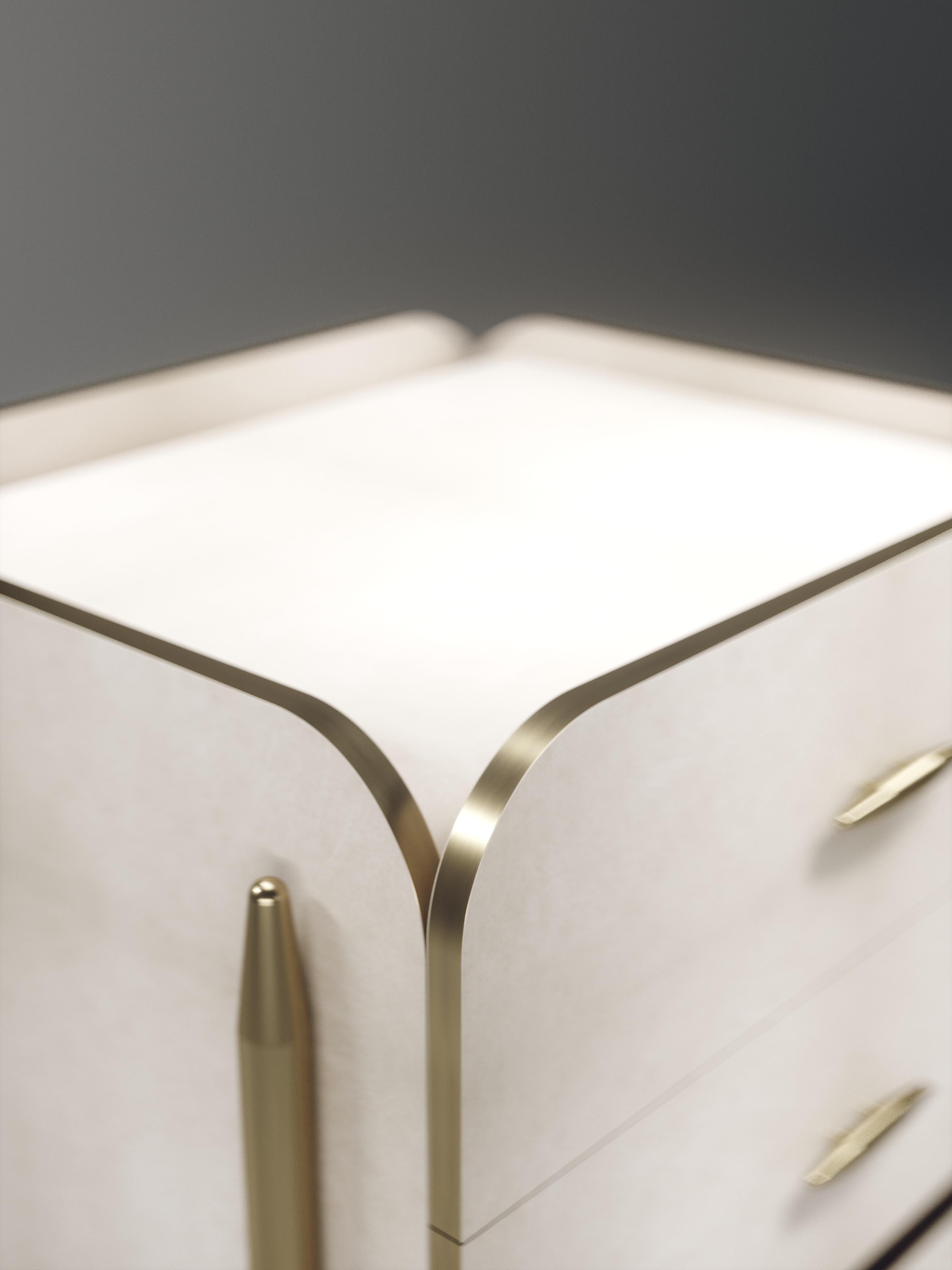 The Dandy square bedside table by Kifu Paris is an elegant and a luxurious home accent, inlaid in cream parchment with bronze-patina brass details. This piece includes 3 drawers total and the interiors are inlaid in gemelina wood veneer. Available