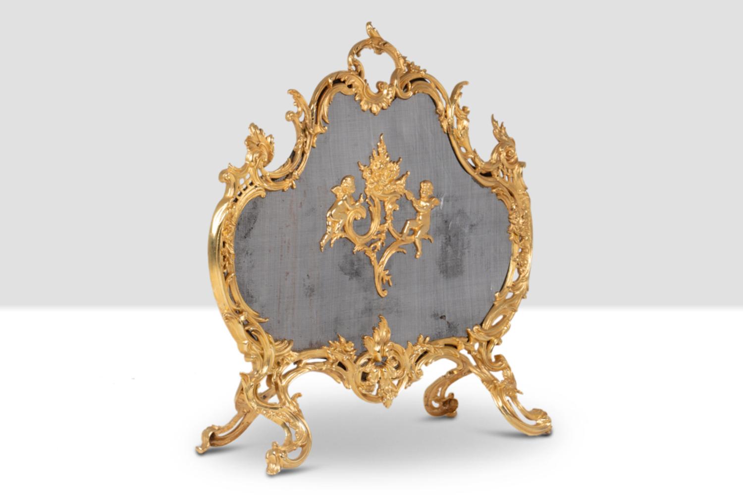 Gilt bronze fire screen with scalloped shape and rocaille decoration of plants, acanthus leaves, shells and foliage. Decorated with cherubs in the central part, standing turned near stylized flames.

French work realized circa 1880.

Reference: