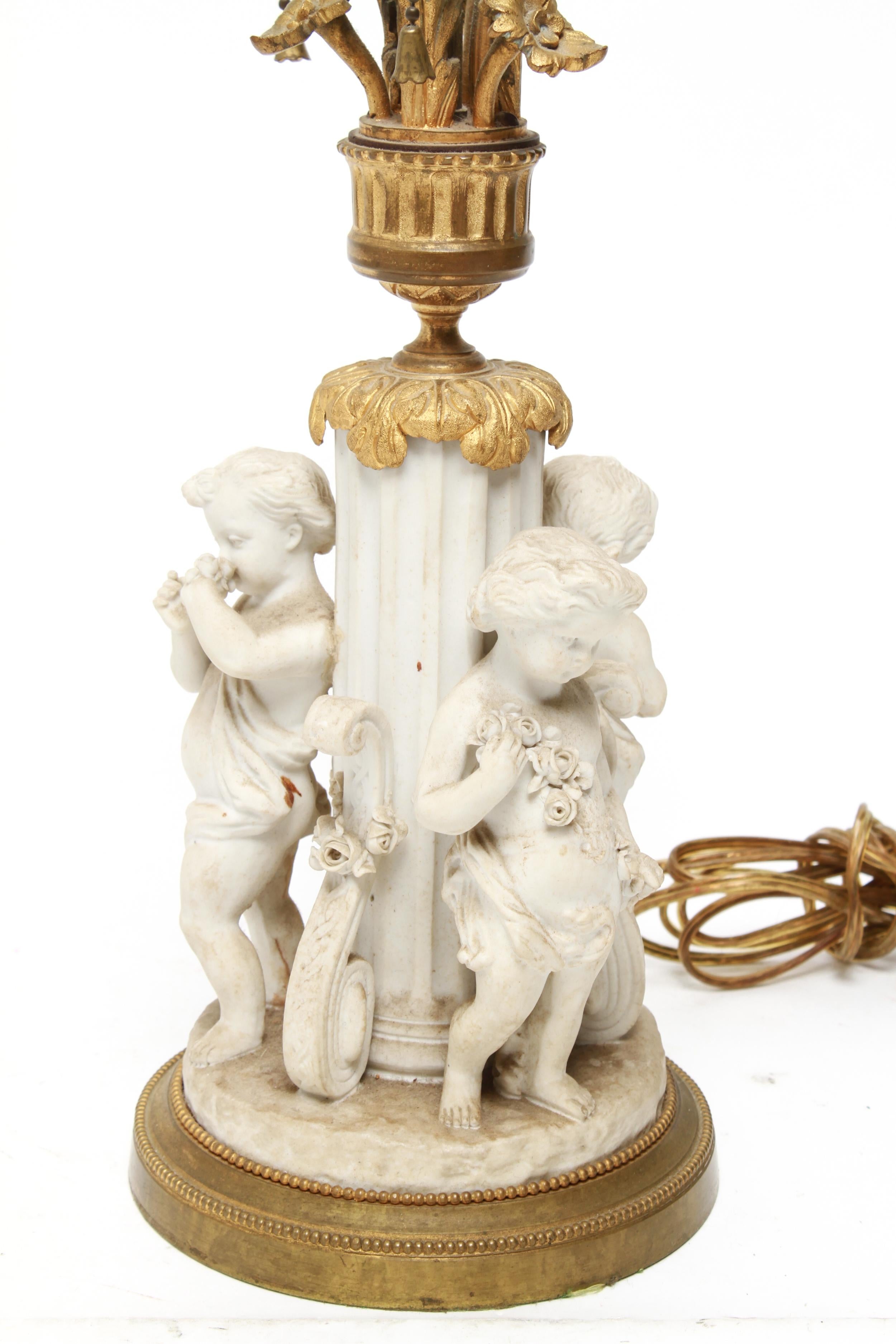 Parian bisque porcelain table lamp with three light sockets above a classical column base surrounded by cherubs and decorative brackets. The top has ormolu mounts. In great vintage condition with an old dark paint mark.