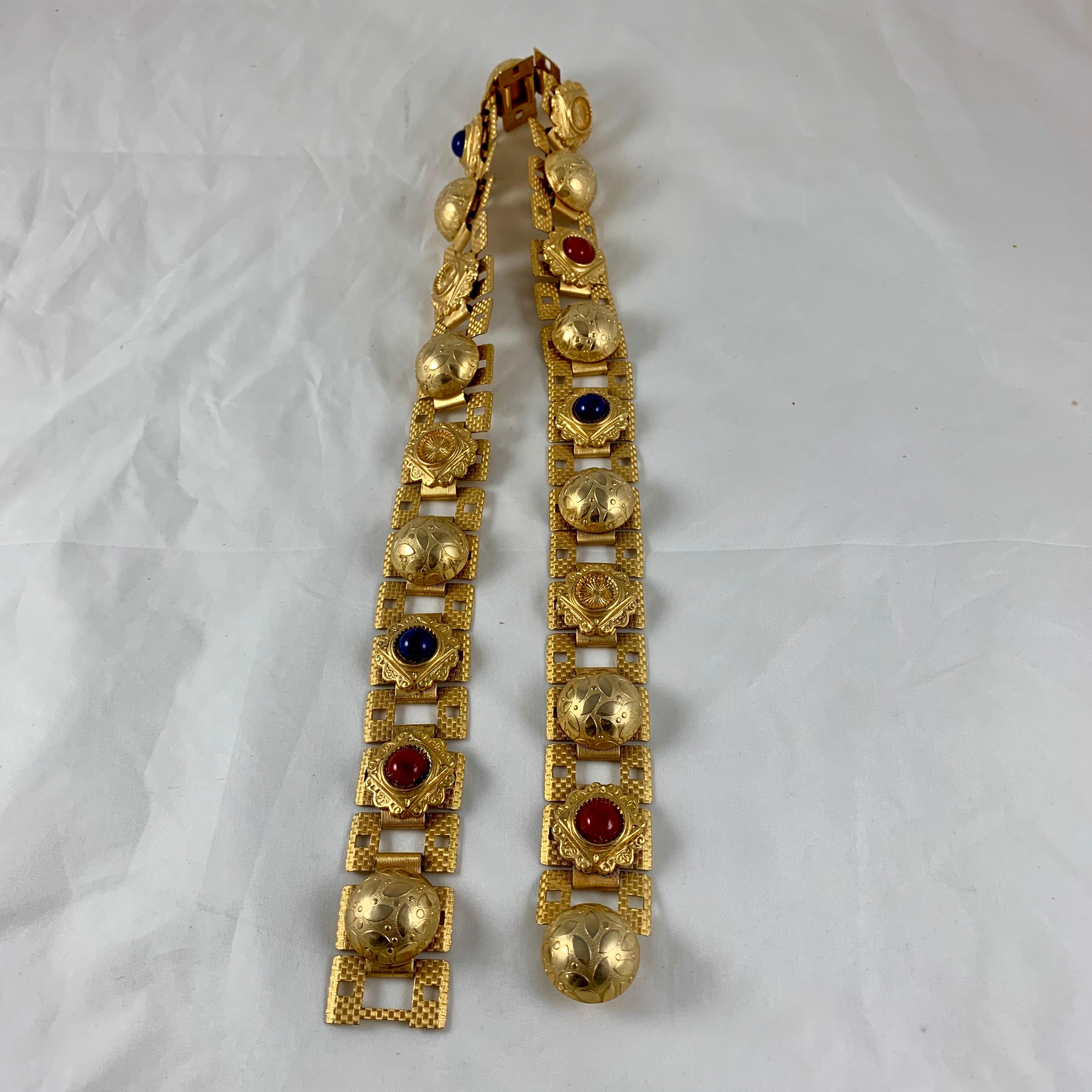 From Paris, France, a 1960s Era belt made of gold-tone metal rectangular links with applied medallions, and bakelite 'jewels'. Unusual and impactful! Heavy and very well made.

Assembled by hand, the links show an impressed, cross-hatched textured