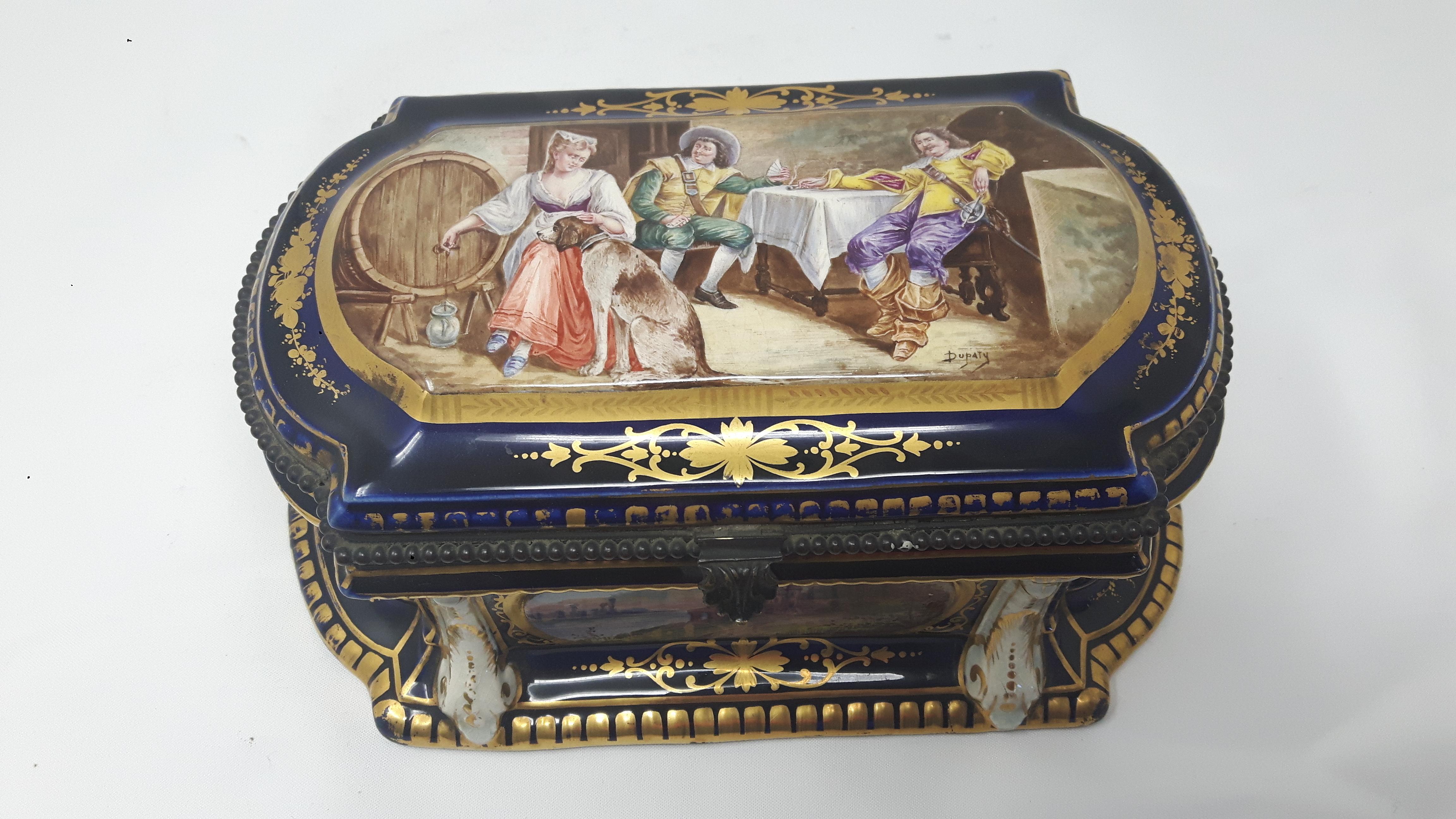 Boîte à bijoux en porcelaine de Paris peinte à la main dans le style de Sèvres avec des cartouches représentant une scène de taverne médiévale et des scènes de campagne. La boîte est fortement dorée avec des guirlandes à la manière du XVIIIe