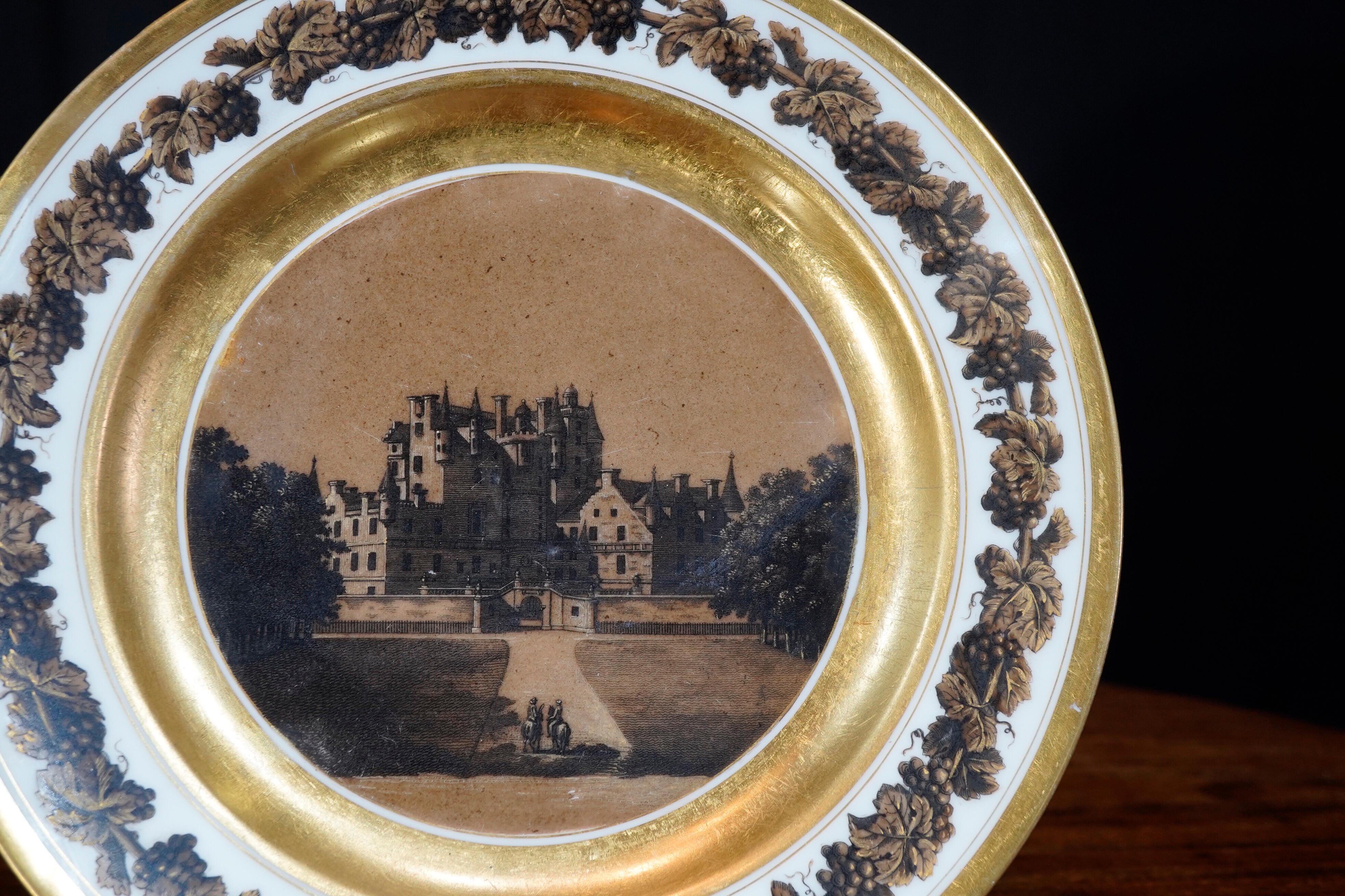 Unusual Paris porcelain plate, printed and painted with a sepia view of an English country house, the details highlighted in gold, the borders with a ‘bronze’ effect fruiting vine wreath within gild line borders.

Marked to the back “Chateau de