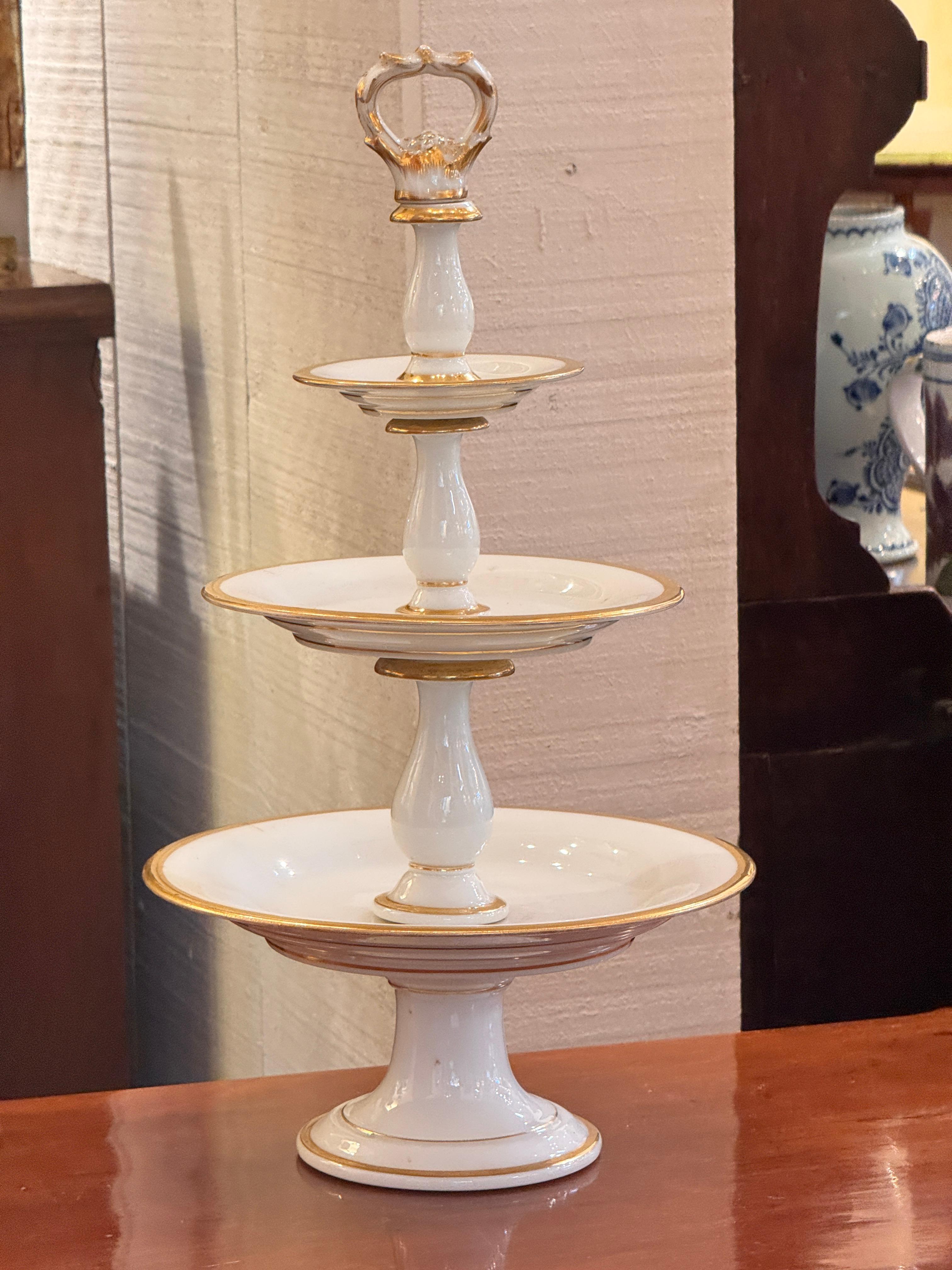 Un'alzata per dolci in porcellana di Parigi a tre livelli, con delicati dettagli dorati dipinti a mano e una scultorea maniglia finale. Lo smalto bianco e brillante contrasta magnificamente con le rifiniture in oro caldo di ogni gradino,