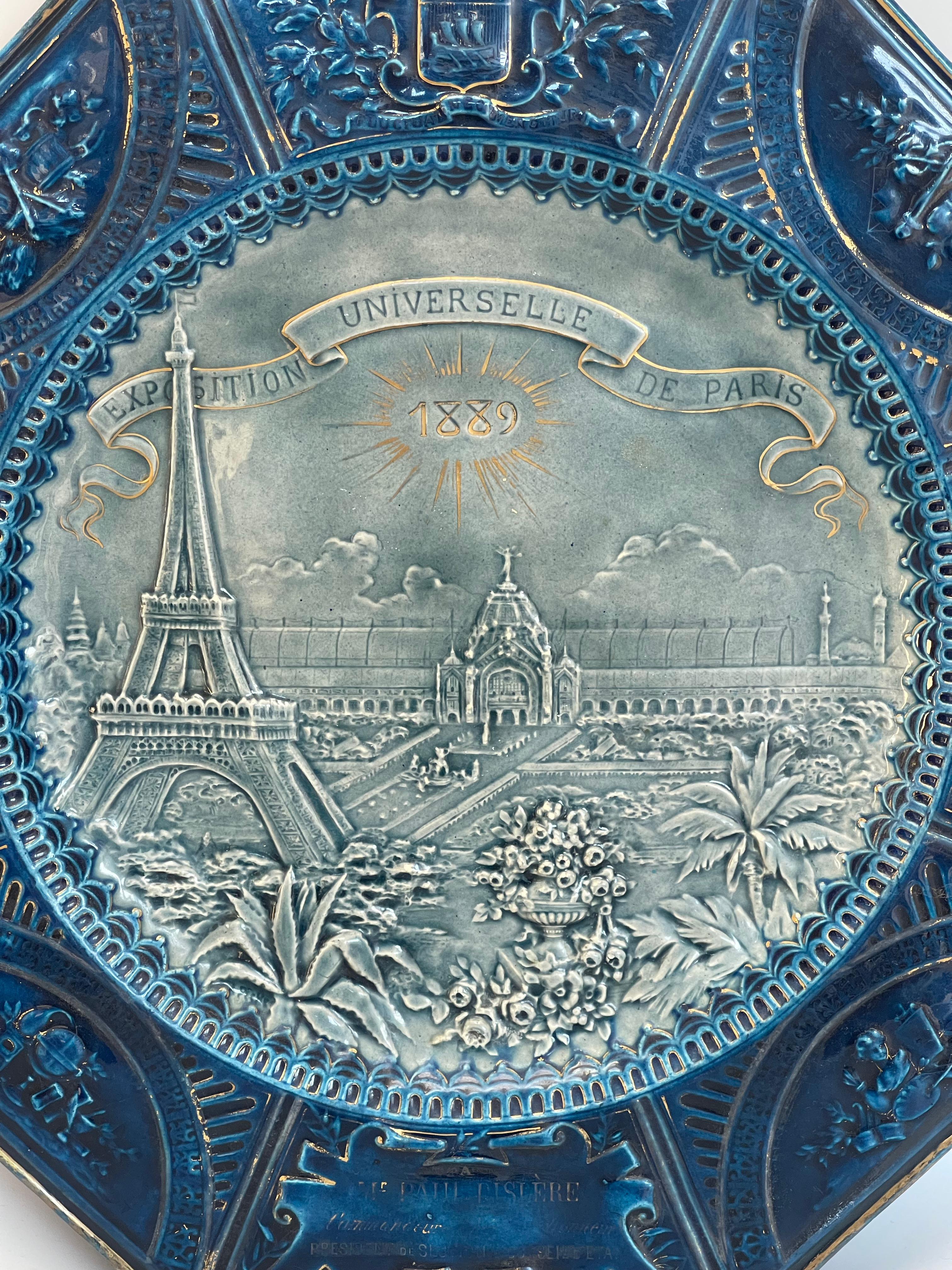 EXPOSITION UNIVERSELLE 1889 Grand plat octogonal en engobe émaillé, l'aile bleue et dorée aux armes de Paris, ornée de cartouches feuillagés, de festons, d'attributs des sciences, des arts, de la musique et de l'agriculture, le centre décoré en demi