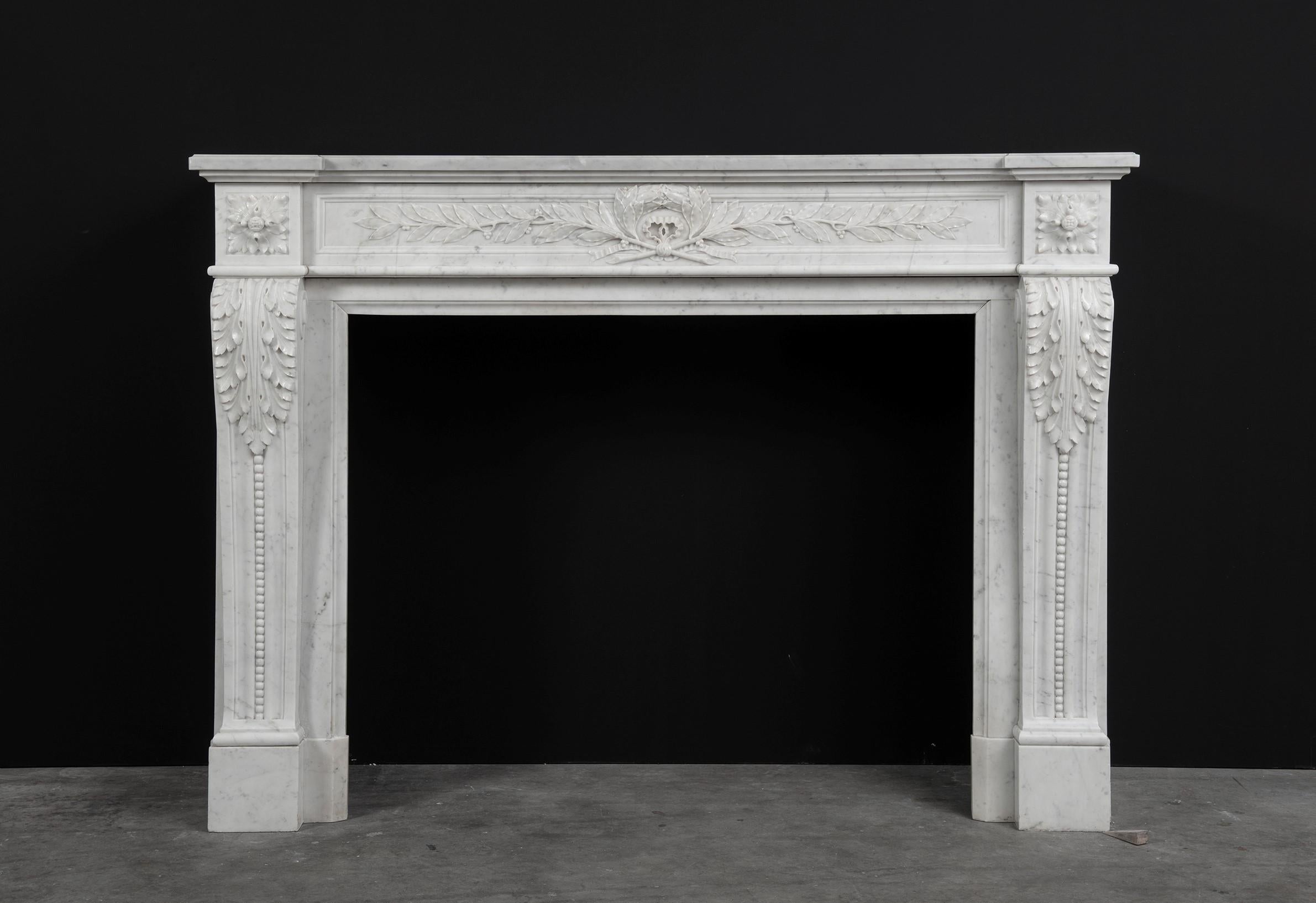 French Antique Louis XVI fireplace mantel in white carrara marble.

Strong and well profiled stepped topshelf above a finely carved paneled frieze with beautiful laurel leaves flanked by floral paterae. The scrolled jambes with paneled sides are