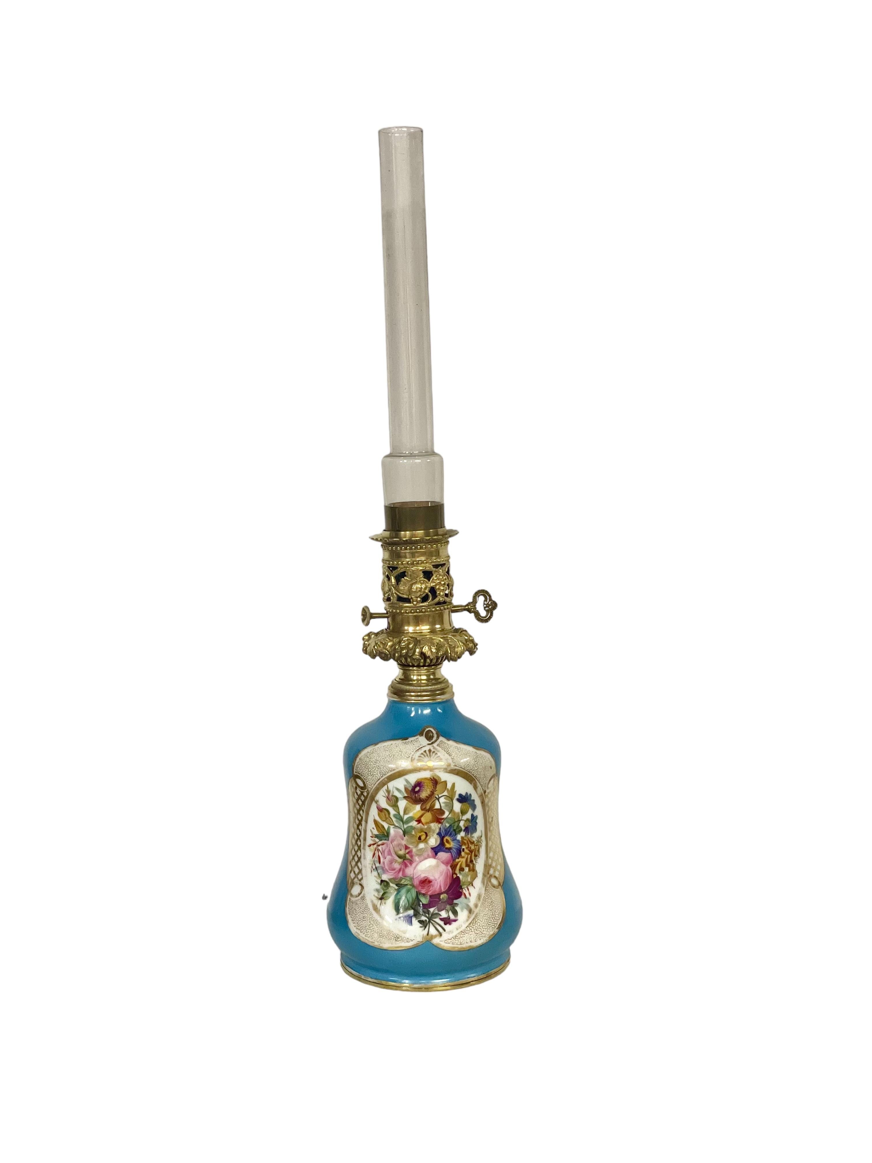 Charmante lampe à huile ancienne en bronze et porcelaine de Paris avec sa cheminée cylindrique en verre d'origine. La base de la lampe est magnifiquement peinte à la main avec un cartouche de fleurs polychromes sur un fond bleu lapis saisissant, et