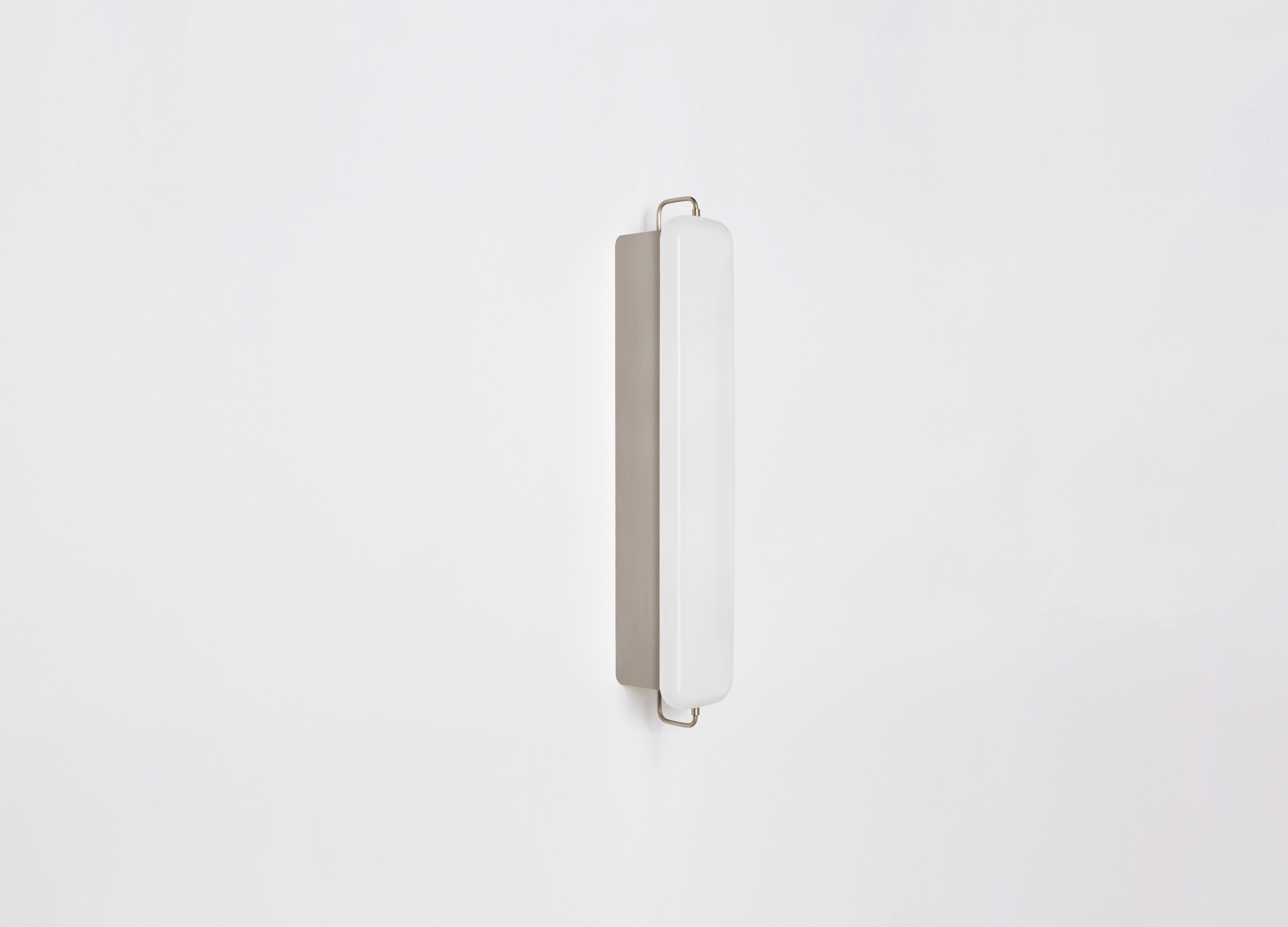 PARK III utilizes an elongated pillow-shaped milk glass form, set against a slender enameled form. The fixture acts as both a light box and wall-washer, spreading light both out and reflecting light against the wall. This fixture is designed to fit