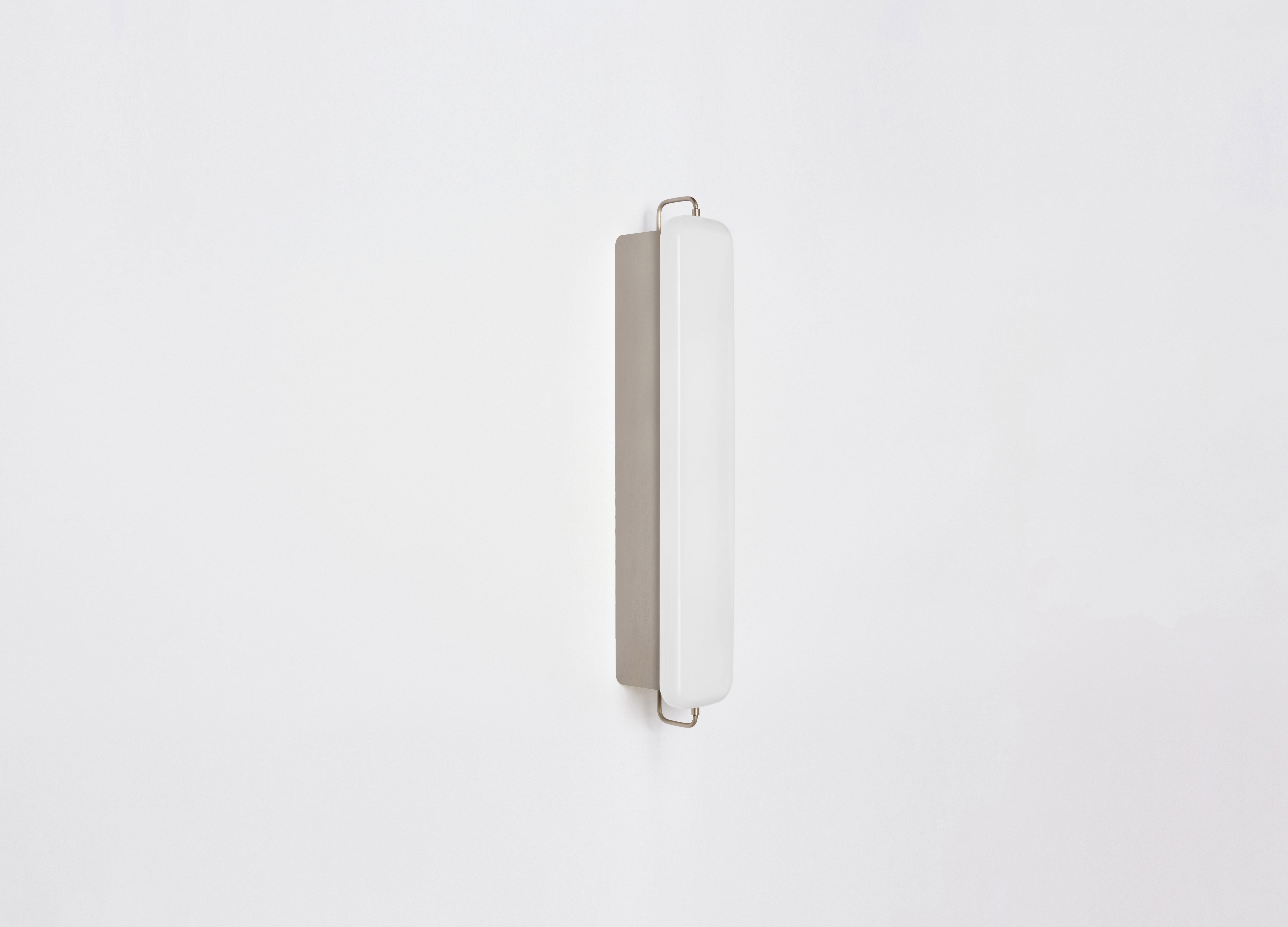 PARK III features a pillow-shaped milk glass shade suspended by delicate metal rods from a slender enameled base. Referencing porcelain fixtures of the pre-war period, the piece acts as both a light box and wall-washer, creating a soft pool of