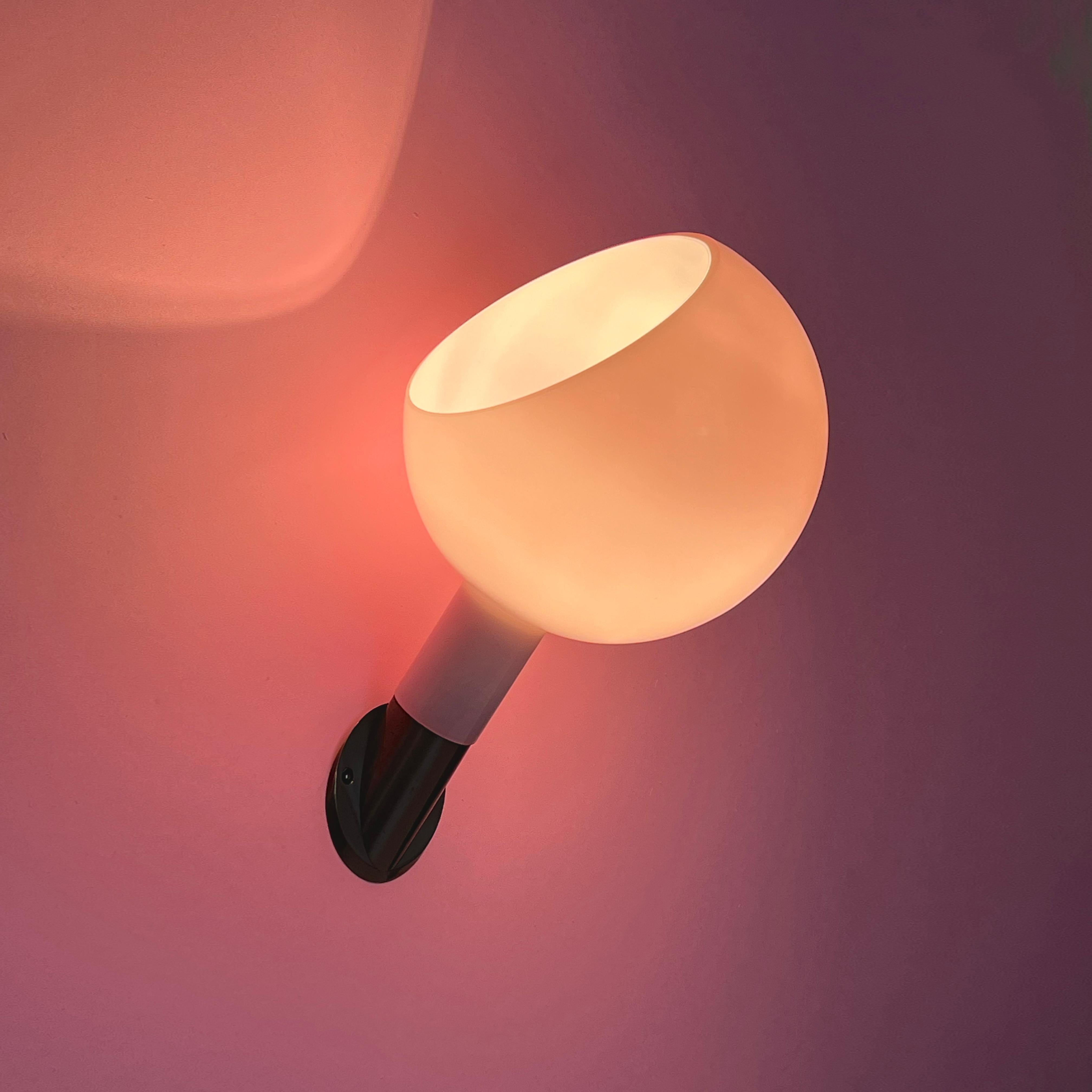 Collaboration de Gae Aulenti et Piero Castiglioni, la lampe Parola présente une fusion harmonieuse de trois techniques distinctes de travail du verre. L'abat-jour réglable est délicatement façonné en verre soufflé opalin, la tige est élégamment