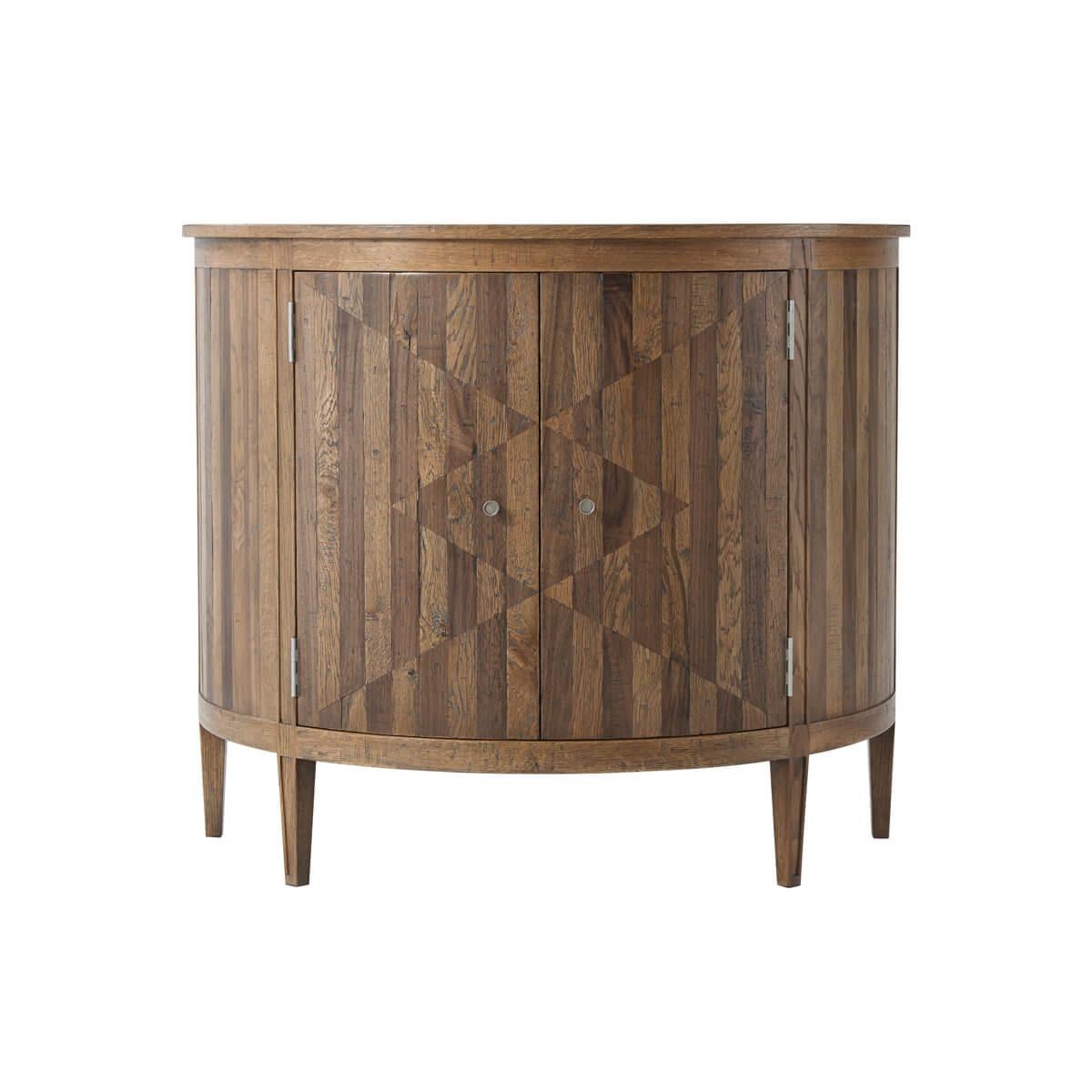 A half-round cabinet with a sunburst inlaid top, finished a natural oak with geometric parquetry doors in oak and walnut, with an adjustable shelf raised on square tapered legs.

Dimensions: 40