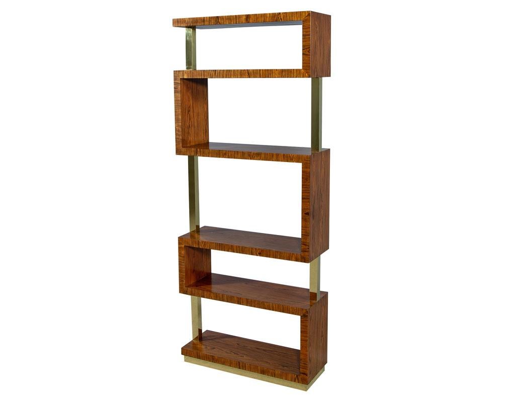 This modern étagère is designed by Kate Spade. The piece is crafted out of six seamless shelves fashioned in an s-shape design. It rests atop a polished brass base and is accented with a polished brass trim. A chic accent piece that adds some flair