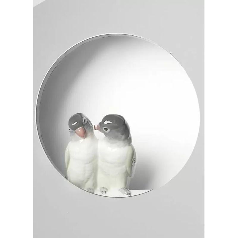 Round mirror with two glossy porcelain parakeets perched on a small circle in the air for home decoration.

Mirror from the Parrot Party collection, based on the contrast between the refined geometric design of the objects' functional forms and