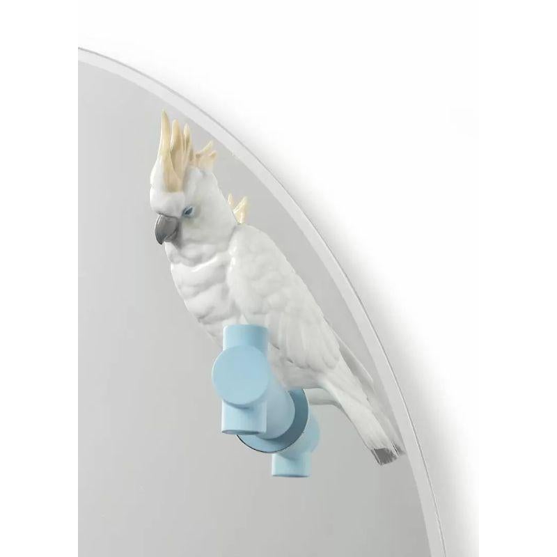 Oval mirror with a glossy porcelain parakeet perched on an original blue branch for home decoration.

Mirror from the Parrot Party collection, based on the contrast between the refined geometric design of the objects' functional forms and the