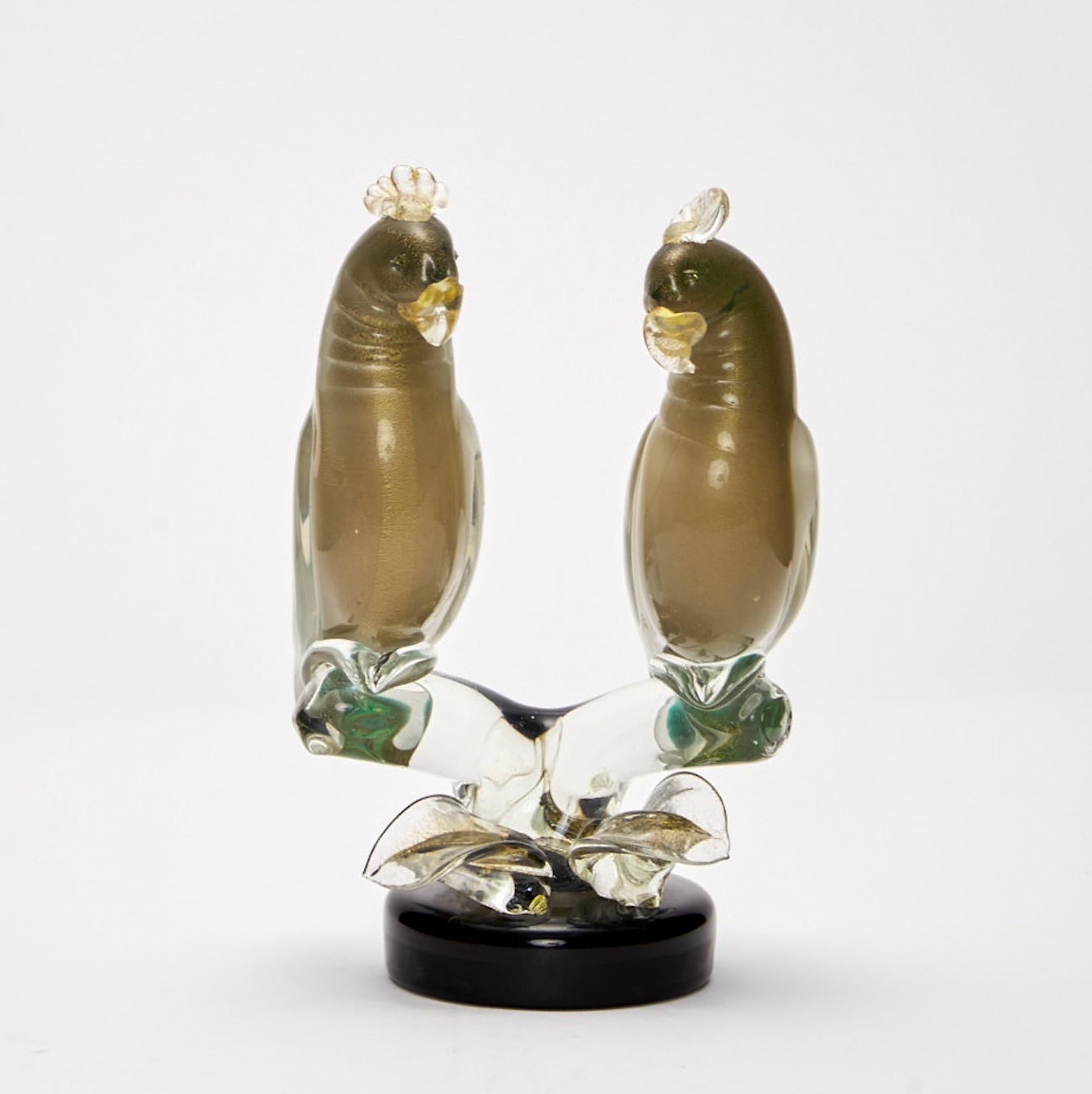 The hand blown Sculpture depicts a pair of parrots poised upon twisted branches. The artist has represented the birds in an opaque dark brown glass decorated internally with gold inclusions and then encased in translucent applied glass. The