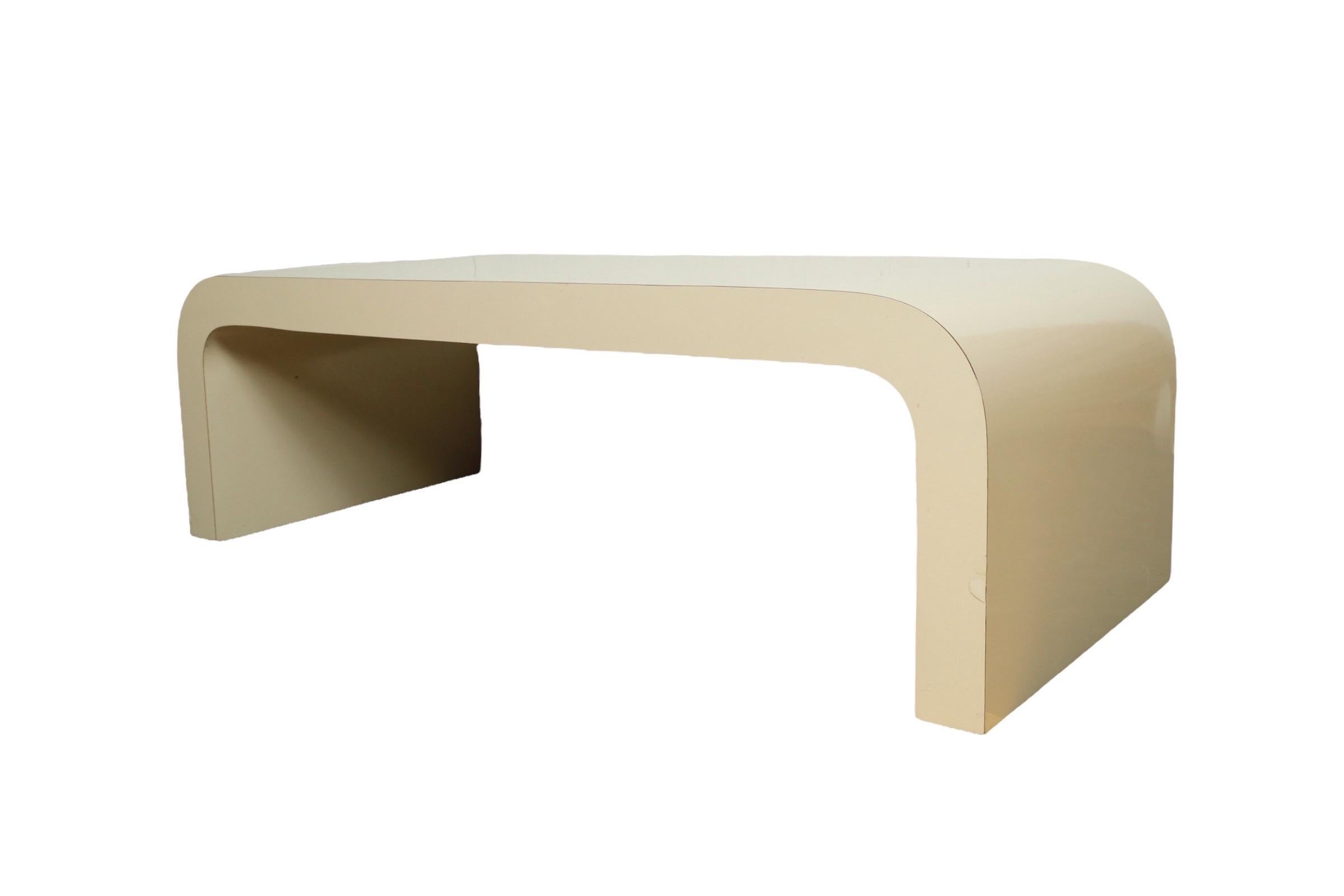Parsons style waterfall coffee table or bench in off white laminate over wood.

USA, circa 1970.

Dimensions: 52.5” L x 22” D x 16.5” H.