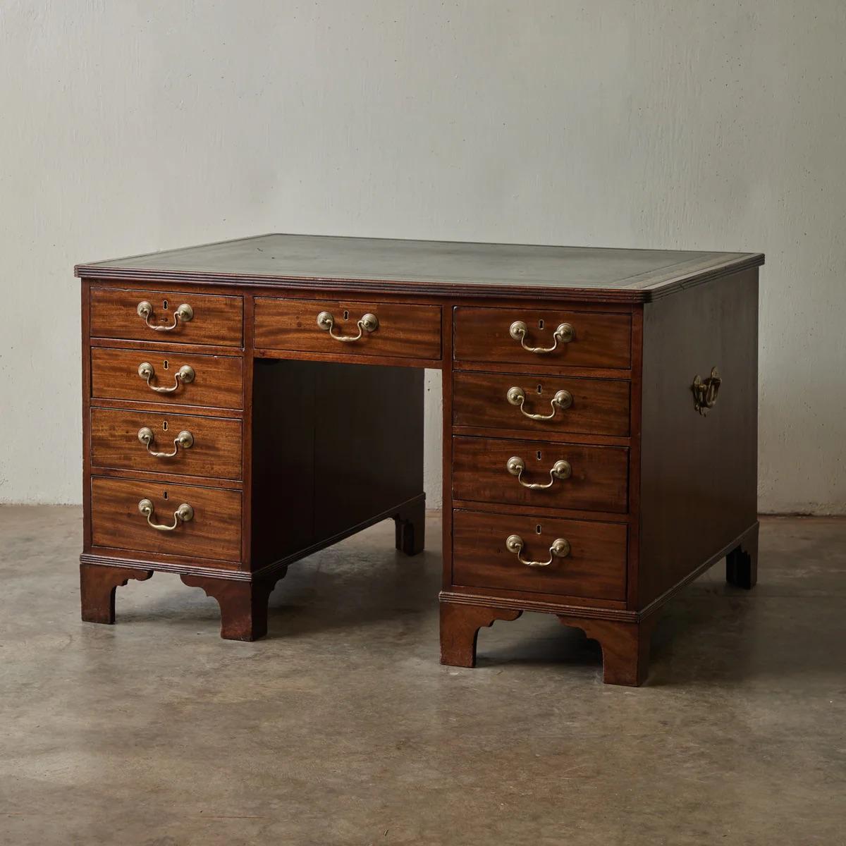 Questo squisito scrittoio in mogano inglese dell'inizio del XIX secolo è caratterizzato da una struttura robusta e da dettagli classici. Il piano in pelle nera modellata, incorniciato da un motivo a chiave greca dorato, offre uno spazio di lavoro