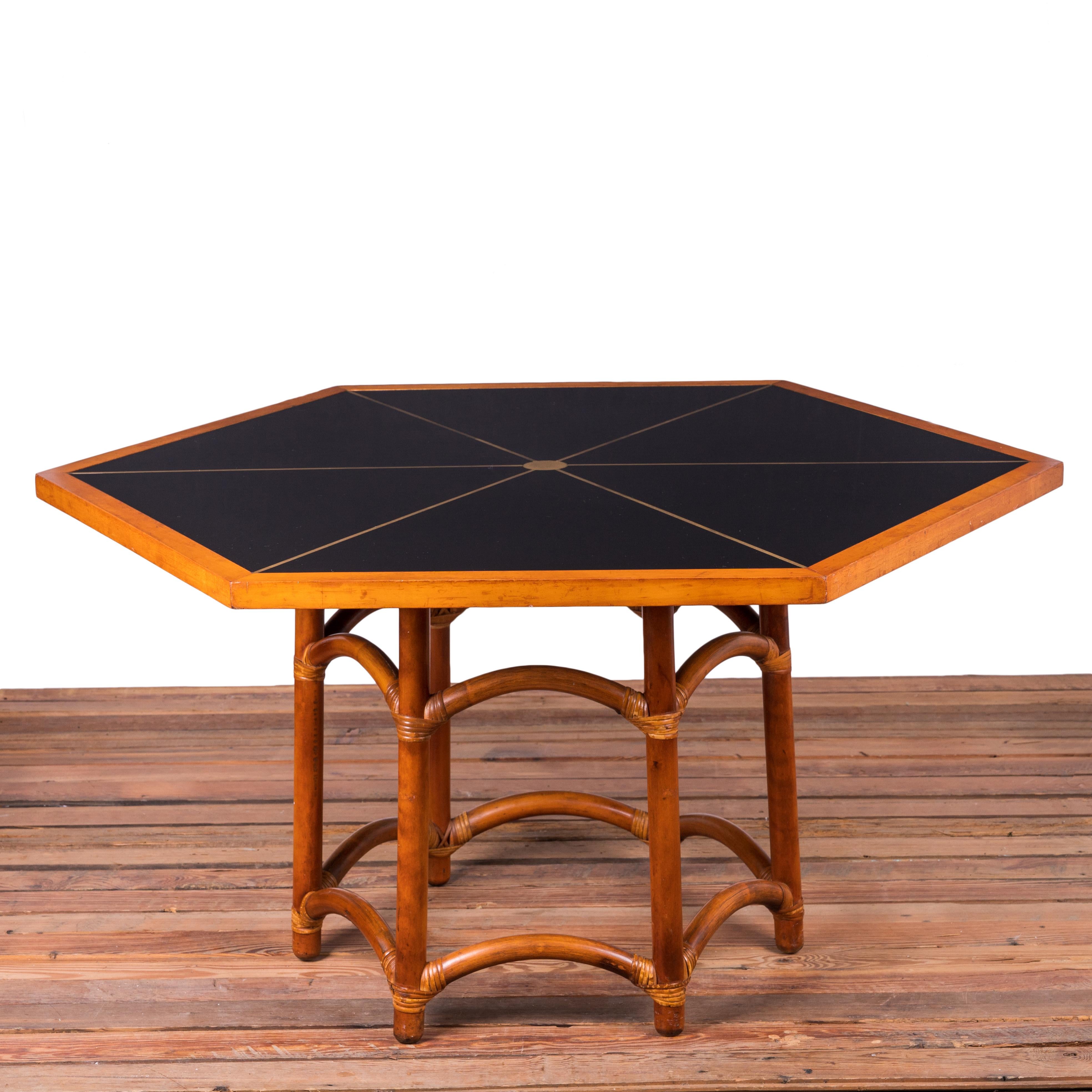 A hexagonal game table designed by Tommi Parzinger for Willow & Reed, Inc., circa 1955.  

Black formica top with inlaid brass in hexagonal maple frame over a wrapped rattan base.

Top measures 44 inches wide by 51 inches at the widest point.  

26